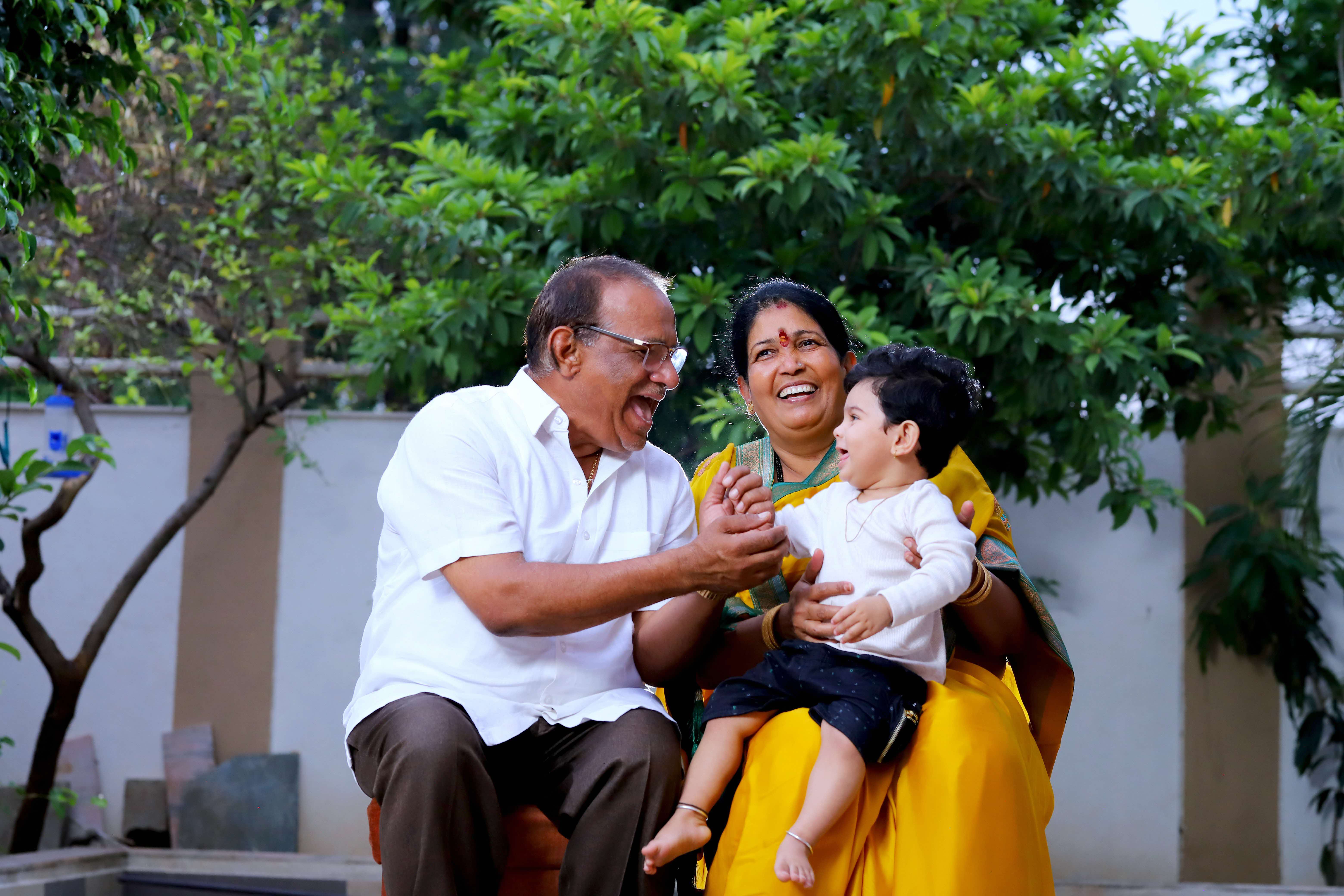 Baby sitting on grandmother's lap, while grandfather is smiling and playing with him