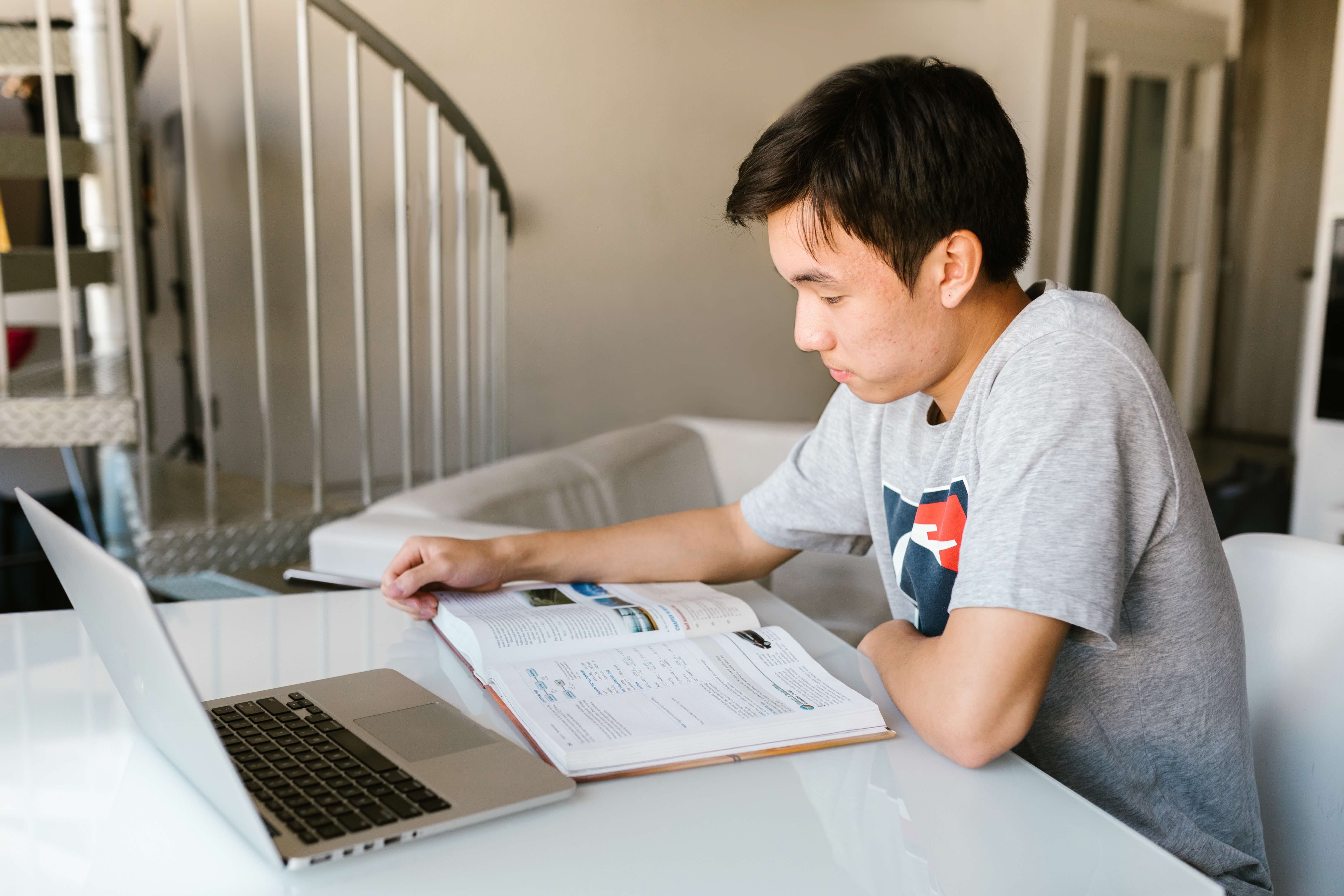 Asian student studying at table with book and laptop open