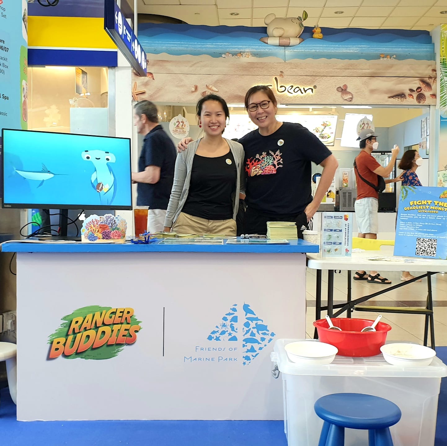 A booth with the "Ranger Buddies" and "Friend of Marine Park" logos, TV screen, pamphlets, and containers on display.