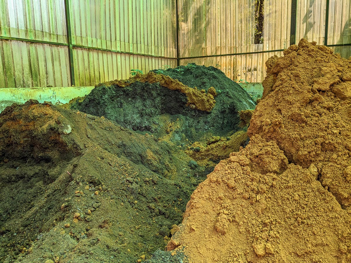 Large piles of soil in various colors inside a metal-walled warehouse with a greenish light.