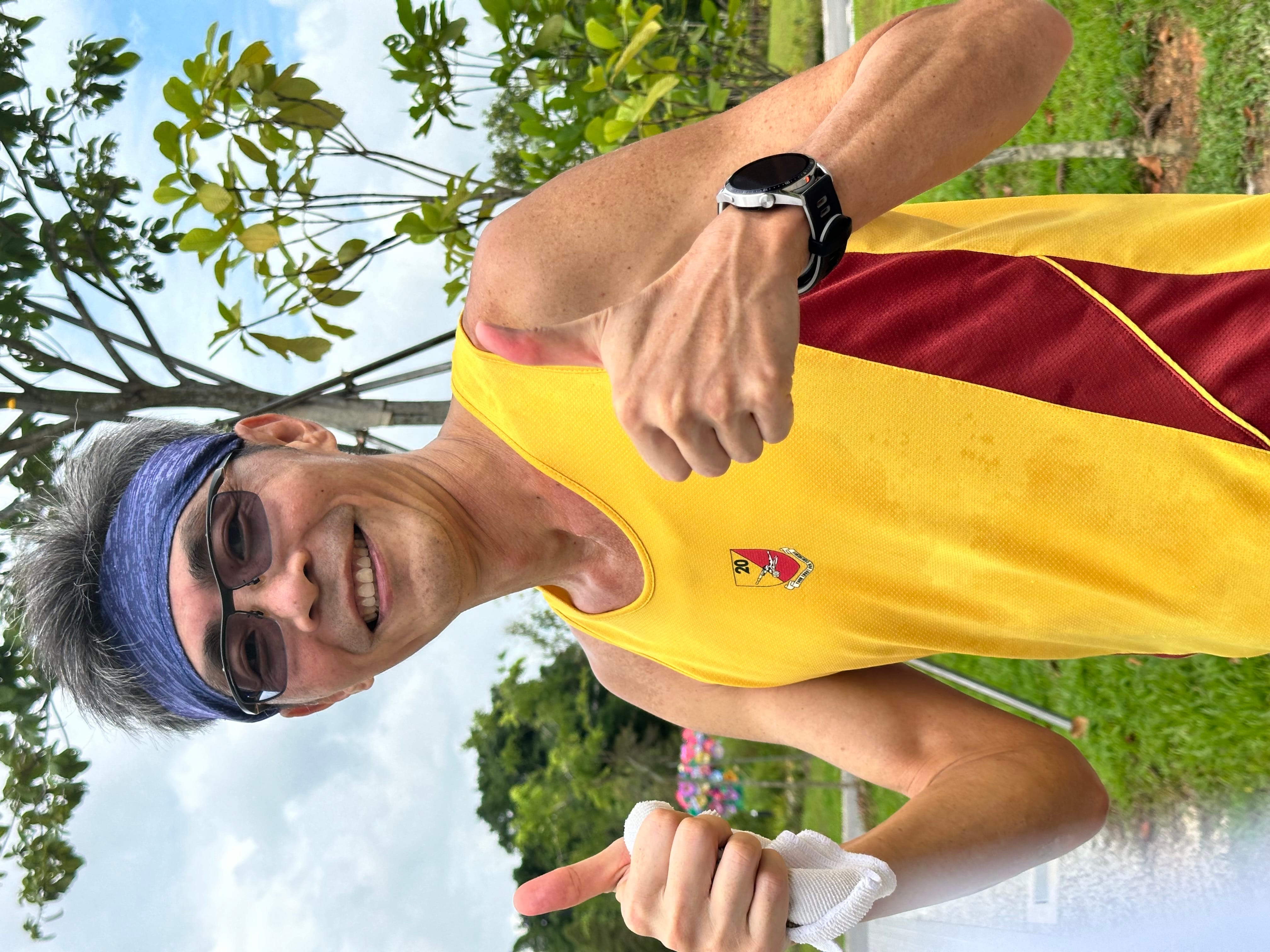 A person wearing a yellow and red sports jersey with a watch shows two thumbs up outdoors.