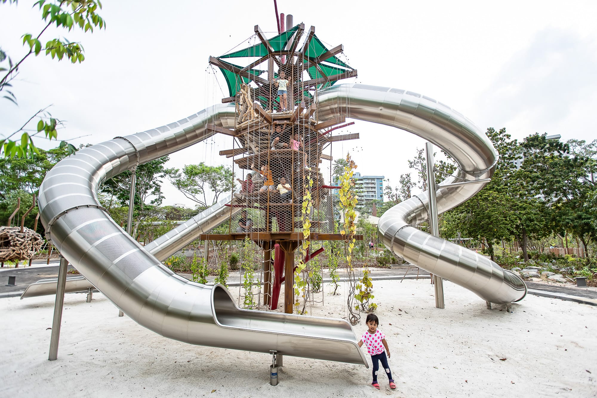 A tall playground structure features multiple twisting slides with several children climbing and playing around it.