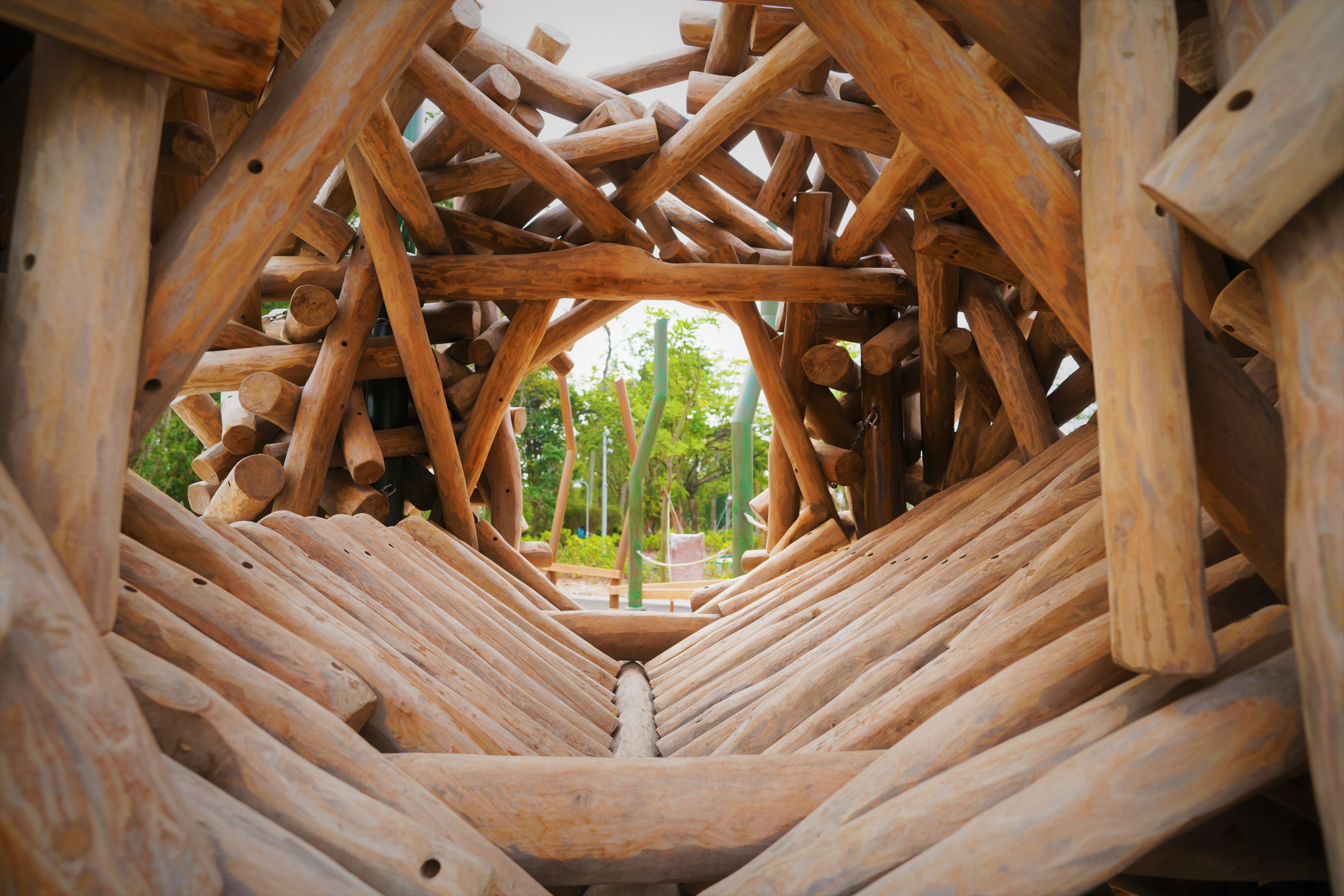 Close-up of a wooden structure made of interconnected logs, with green plants visible through the gaps.
