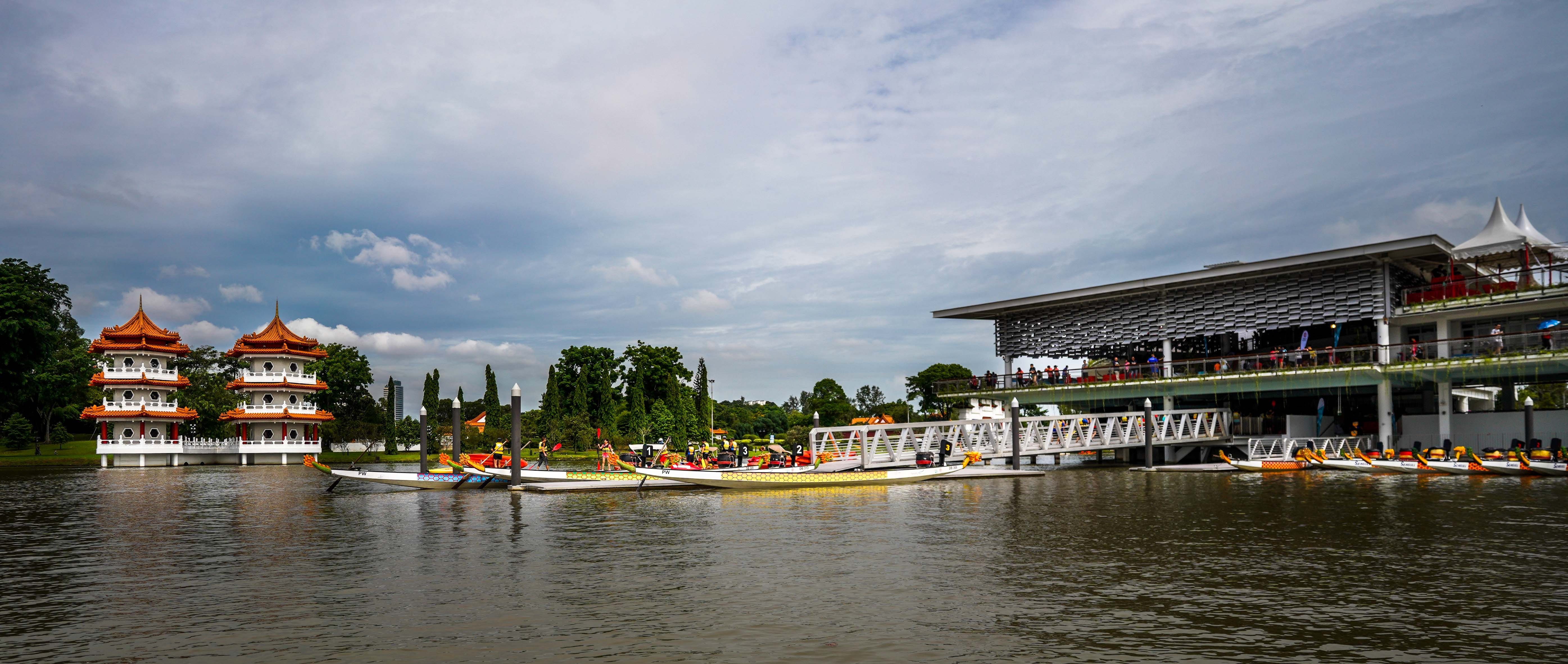 Two pagodas on the left side and a modern building on the right side are next to a large body of water with boats.