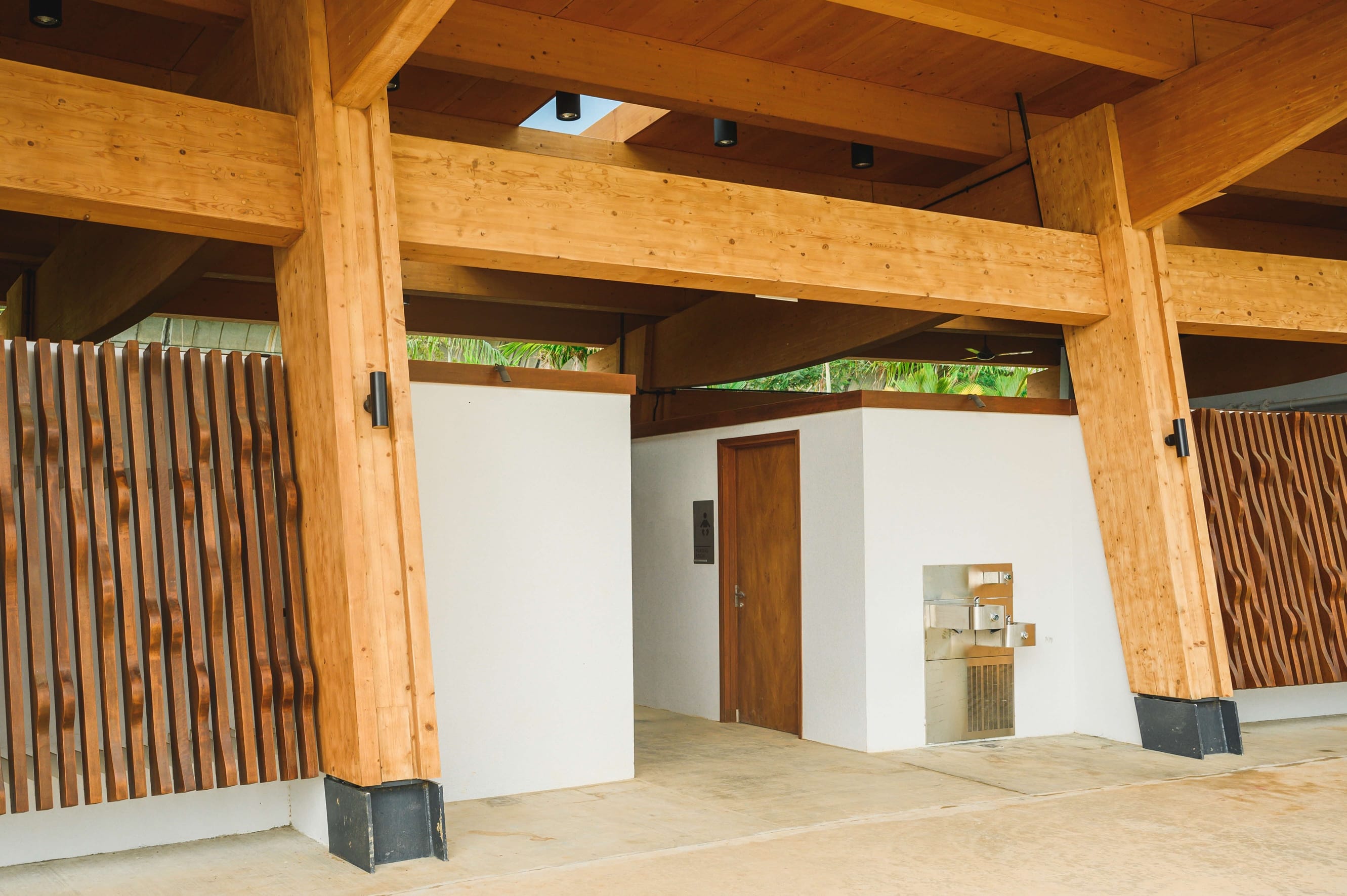 An indoor restroom with wooden accents, white walls, a wooden door, and water fountains on the exterior.