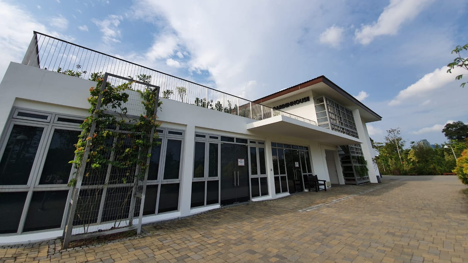 A modern white building labeled "Gardenhouse" with large windows, plants on the balcony, and a clear sky above.