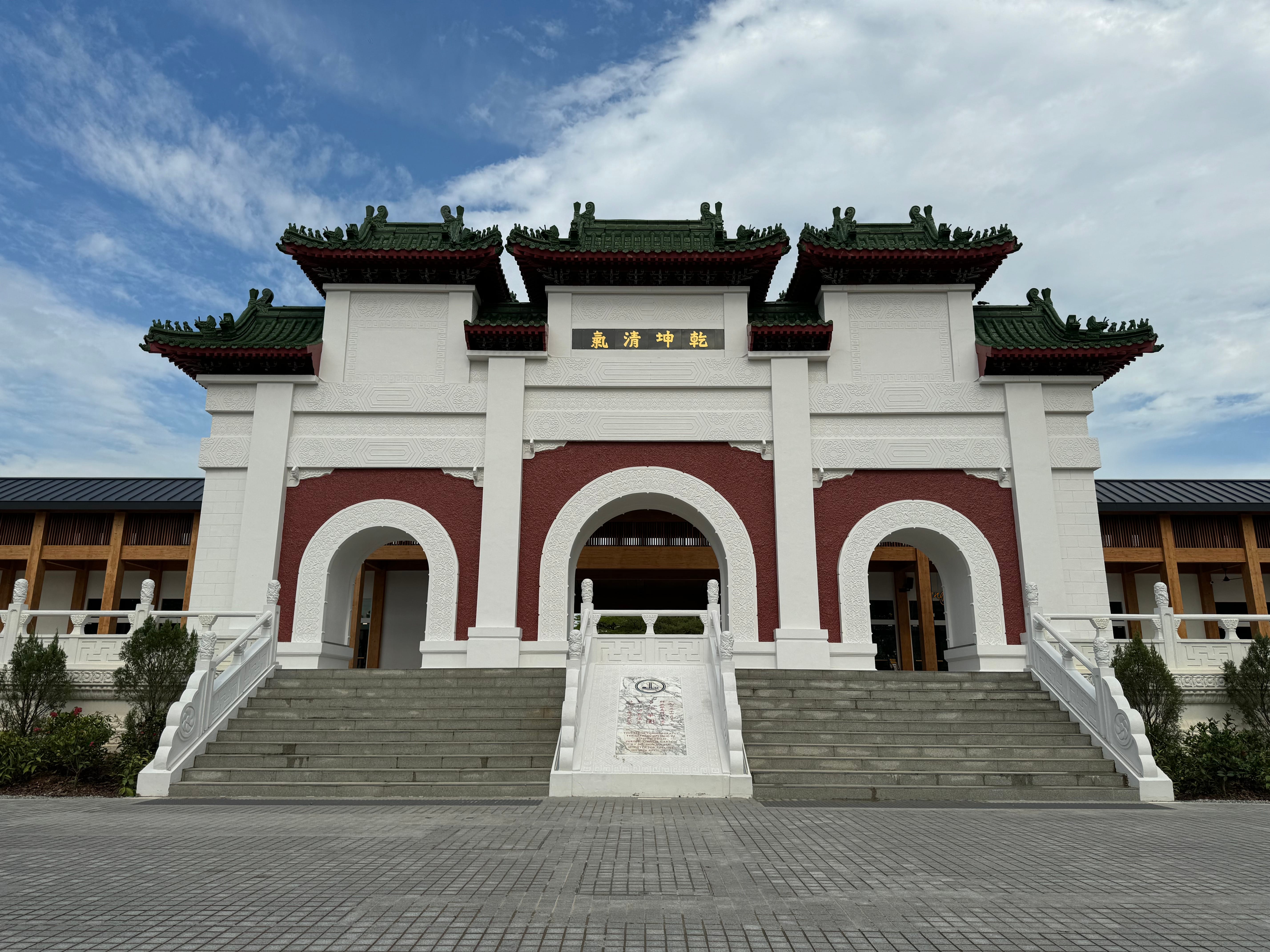 Stone steps lead to a building with three green-tiled pagoda roofs, arches, and Chinese characters on a sign.