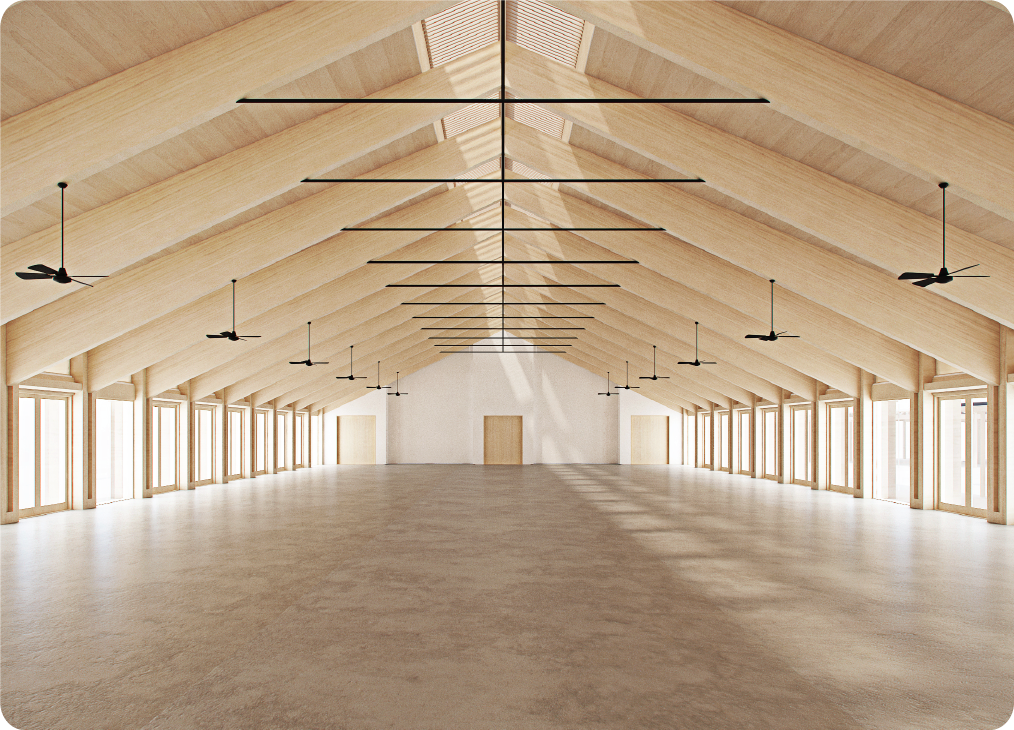A large, airy wooden hall with high, triangular beams, numerous windows, ceiling fans, and two doors at the far end.