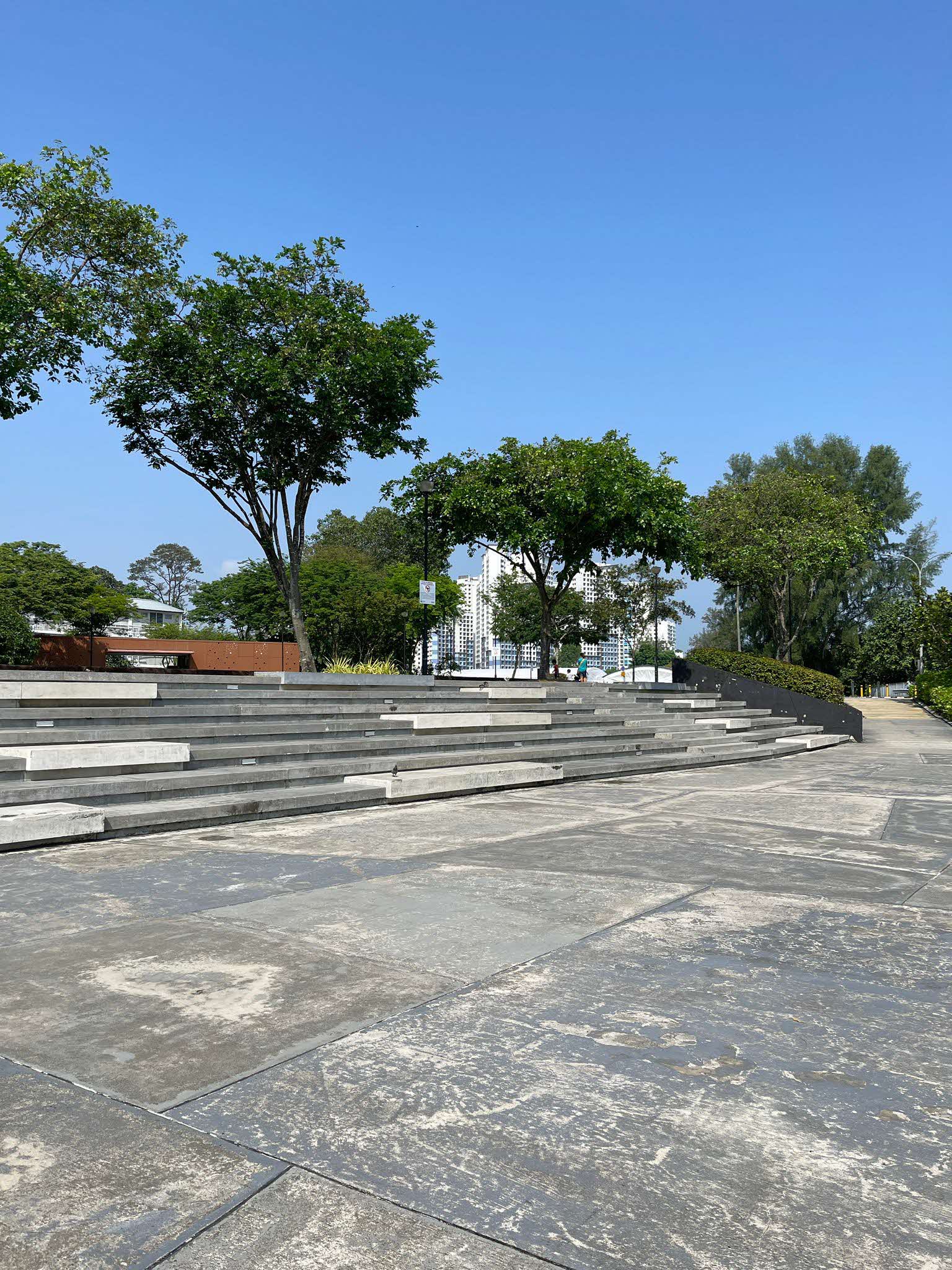 Outdoor stone steps surrounded by trees under a clear blue sky, with buildings visible in the background.