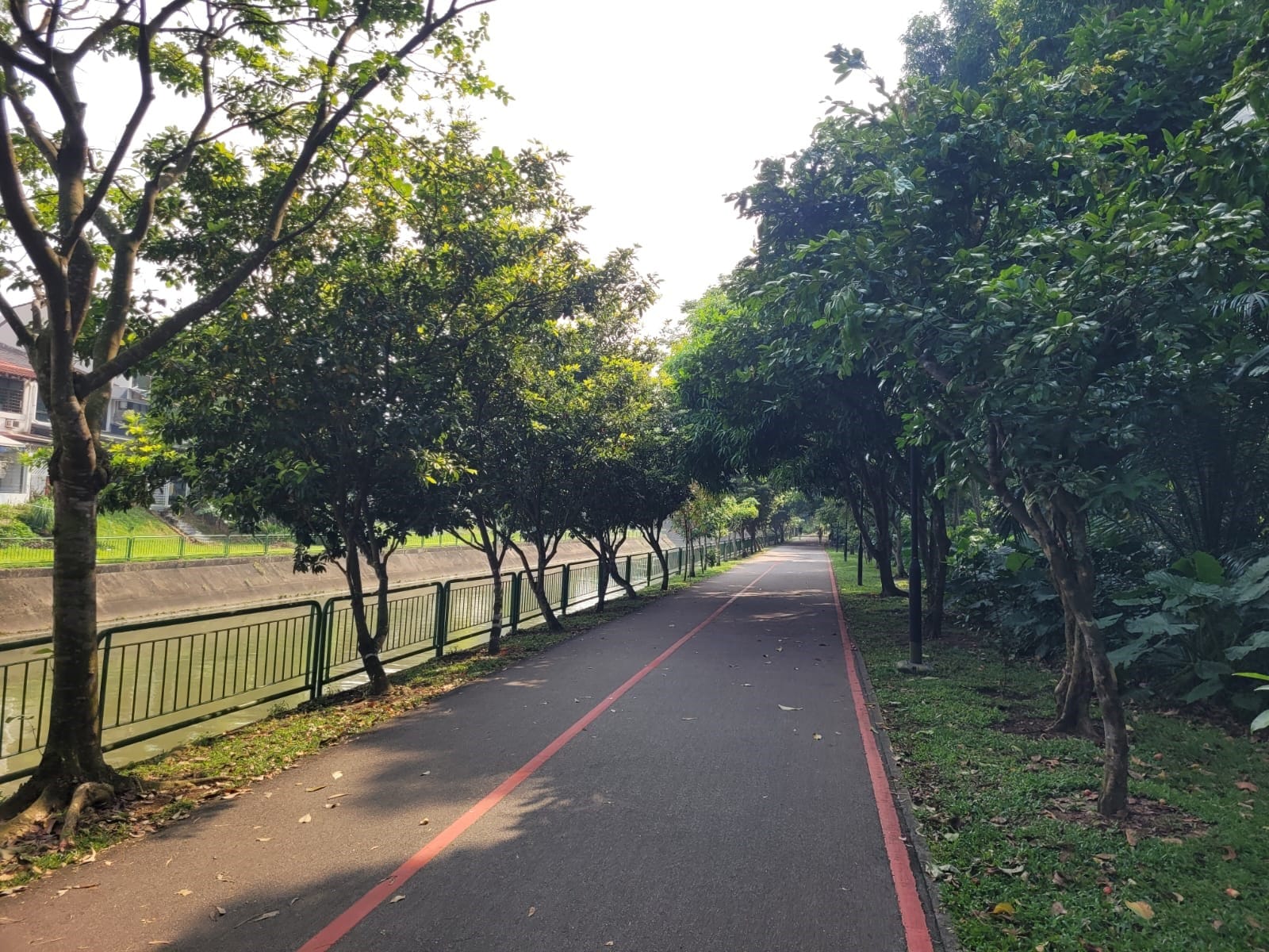 A paved walking path runs beside a canal, lined with trees and greenery on both sides.