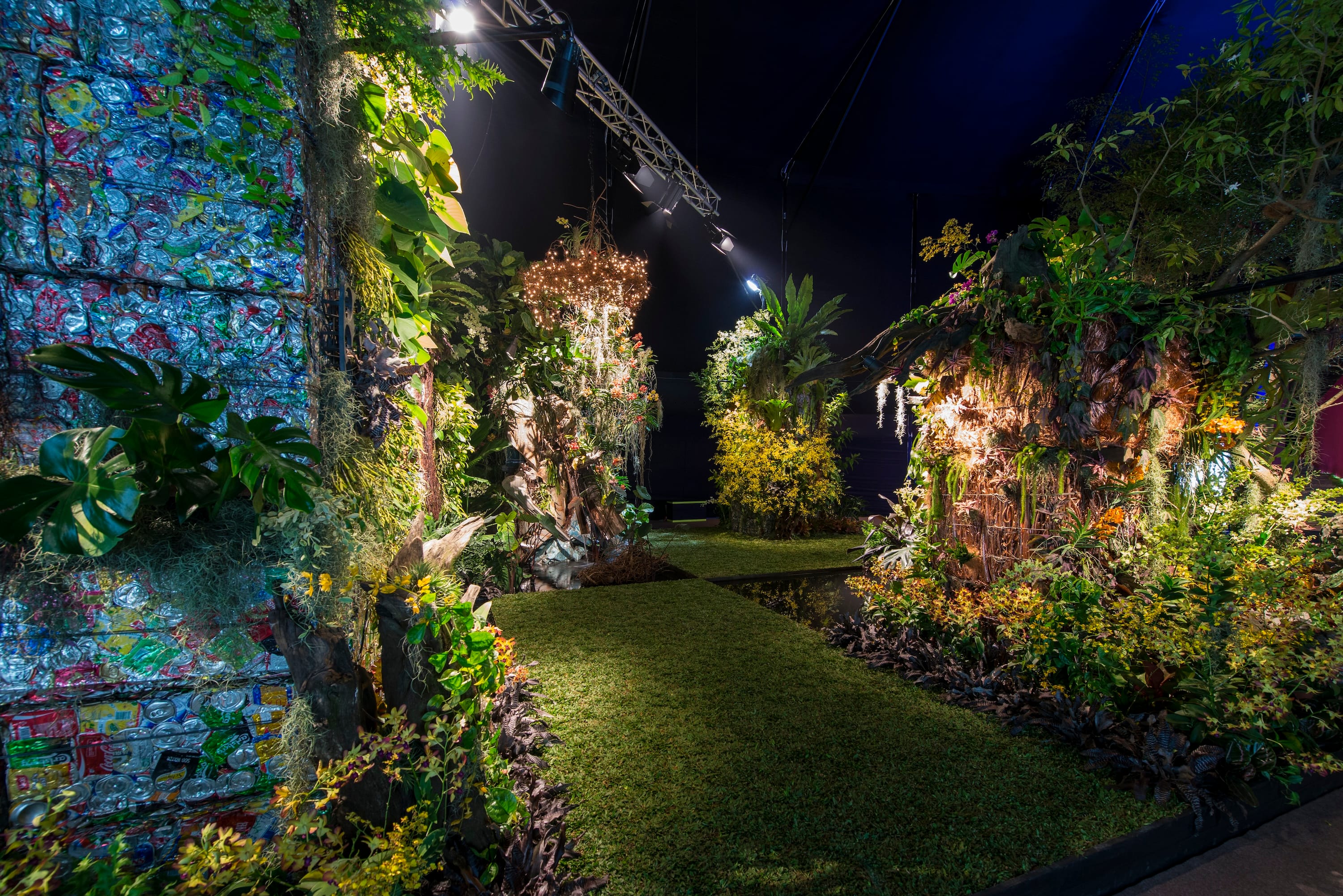 A pathway surrounded by lush greenery and artistic light installations in a vibrant indoor garden setting.