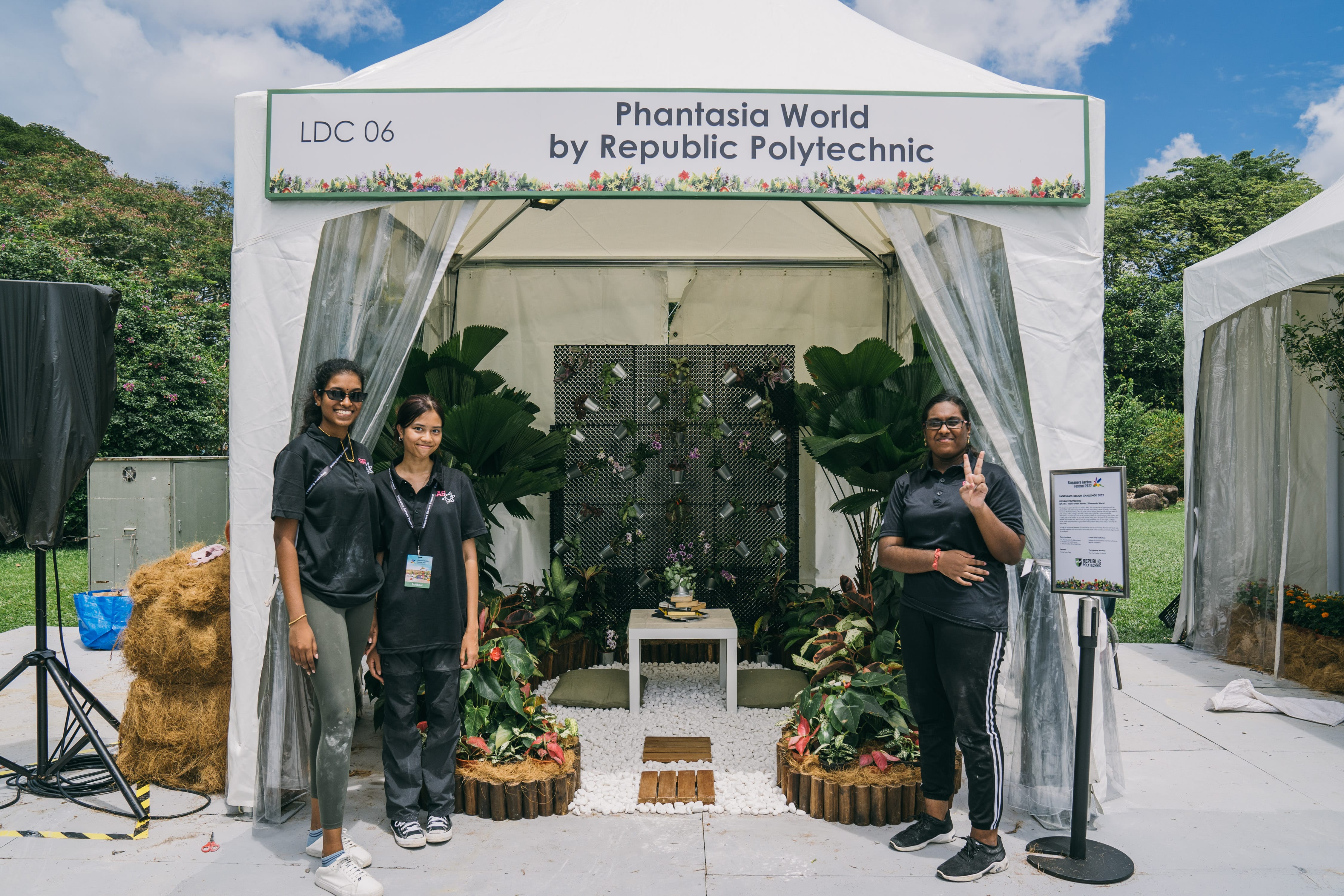 Three people in black shirts posing in front of a decorated tent labeled "Phantasia World by Republic Polytechnic."