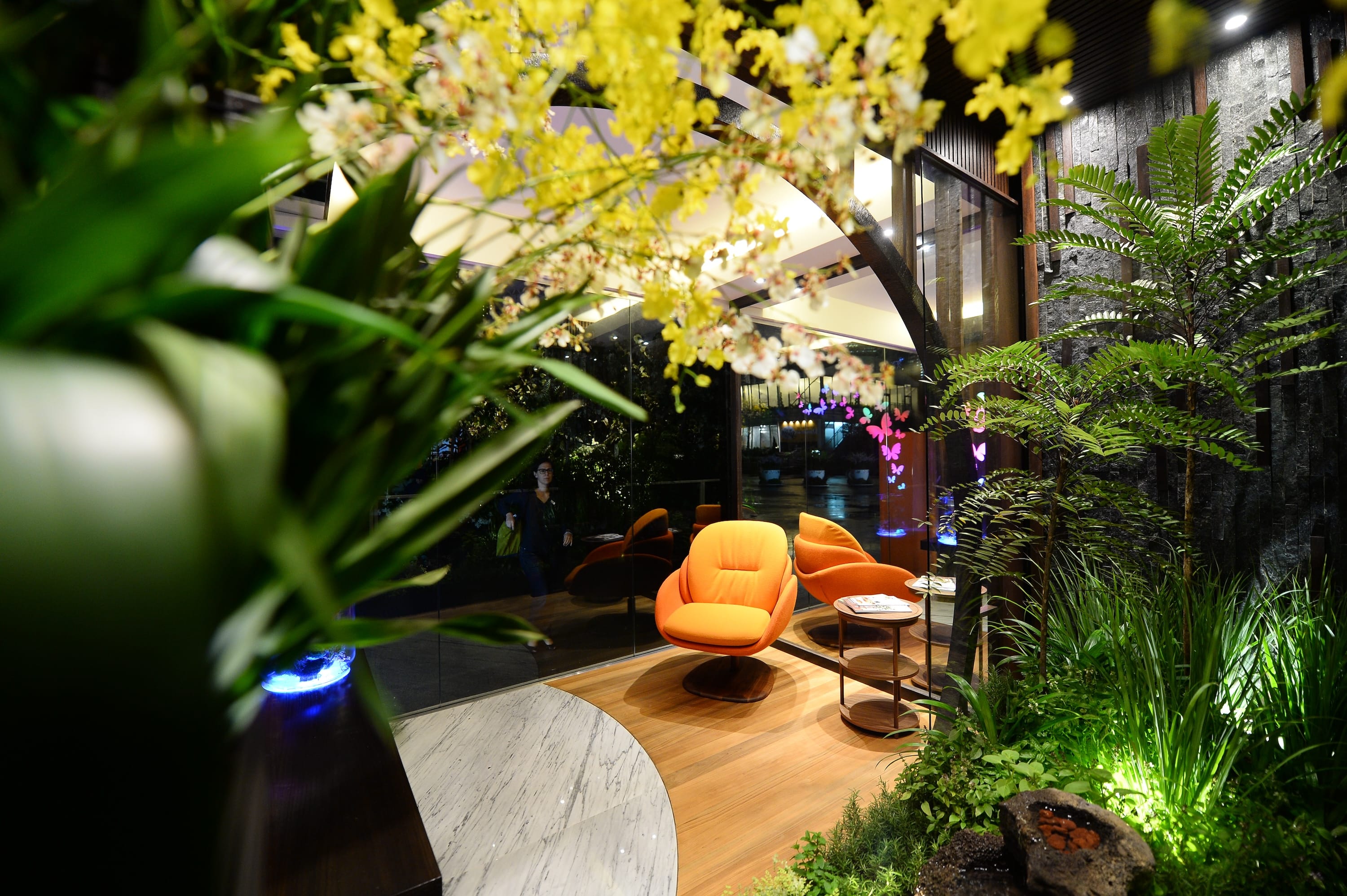 A modern indoor space with bright orange chairs, lush green plants, and decorative yellow flowers in the foreground.