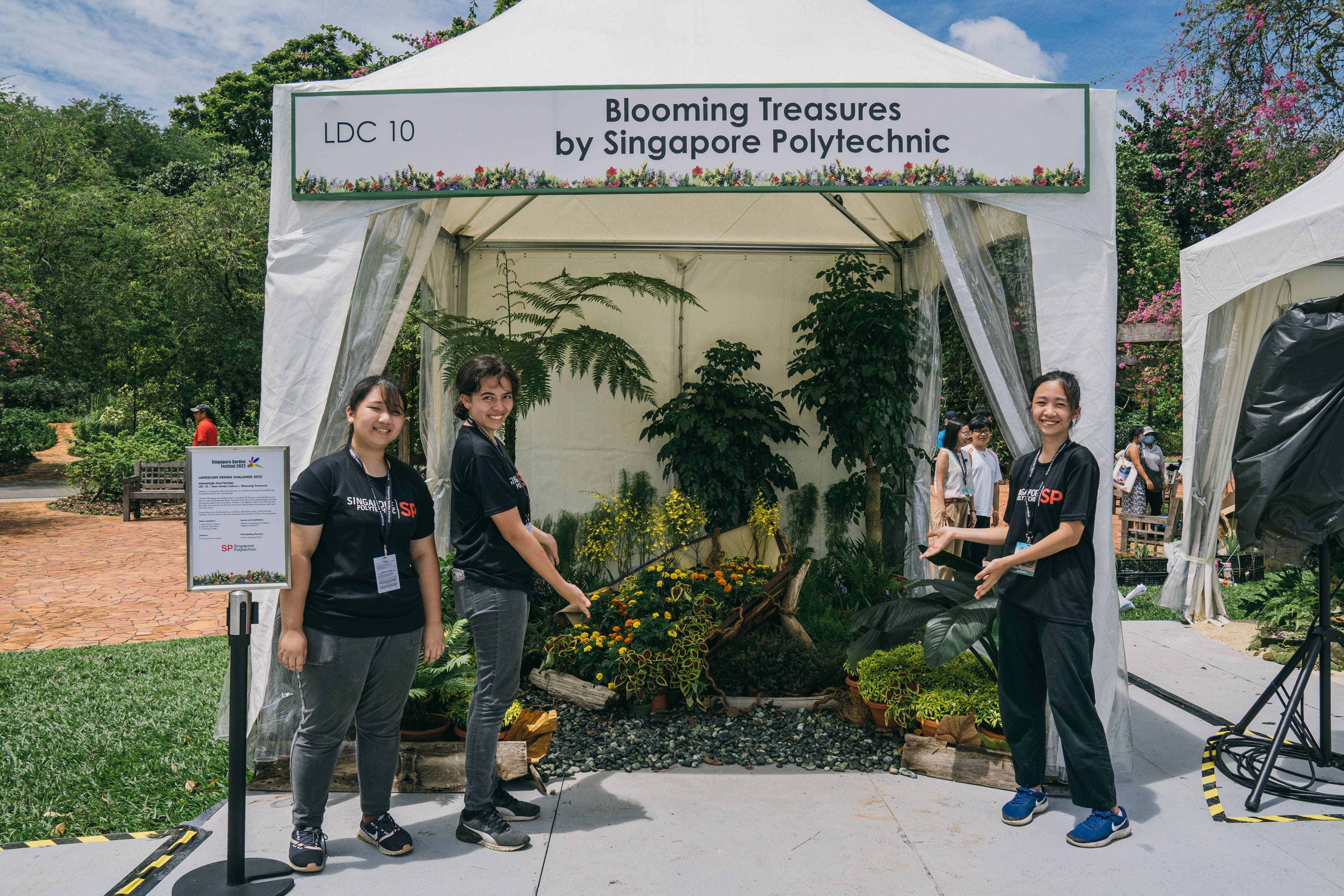 A tent labeled "Blooming Treasures by Singapore Polytechnic" has people standing in front and plants inside.