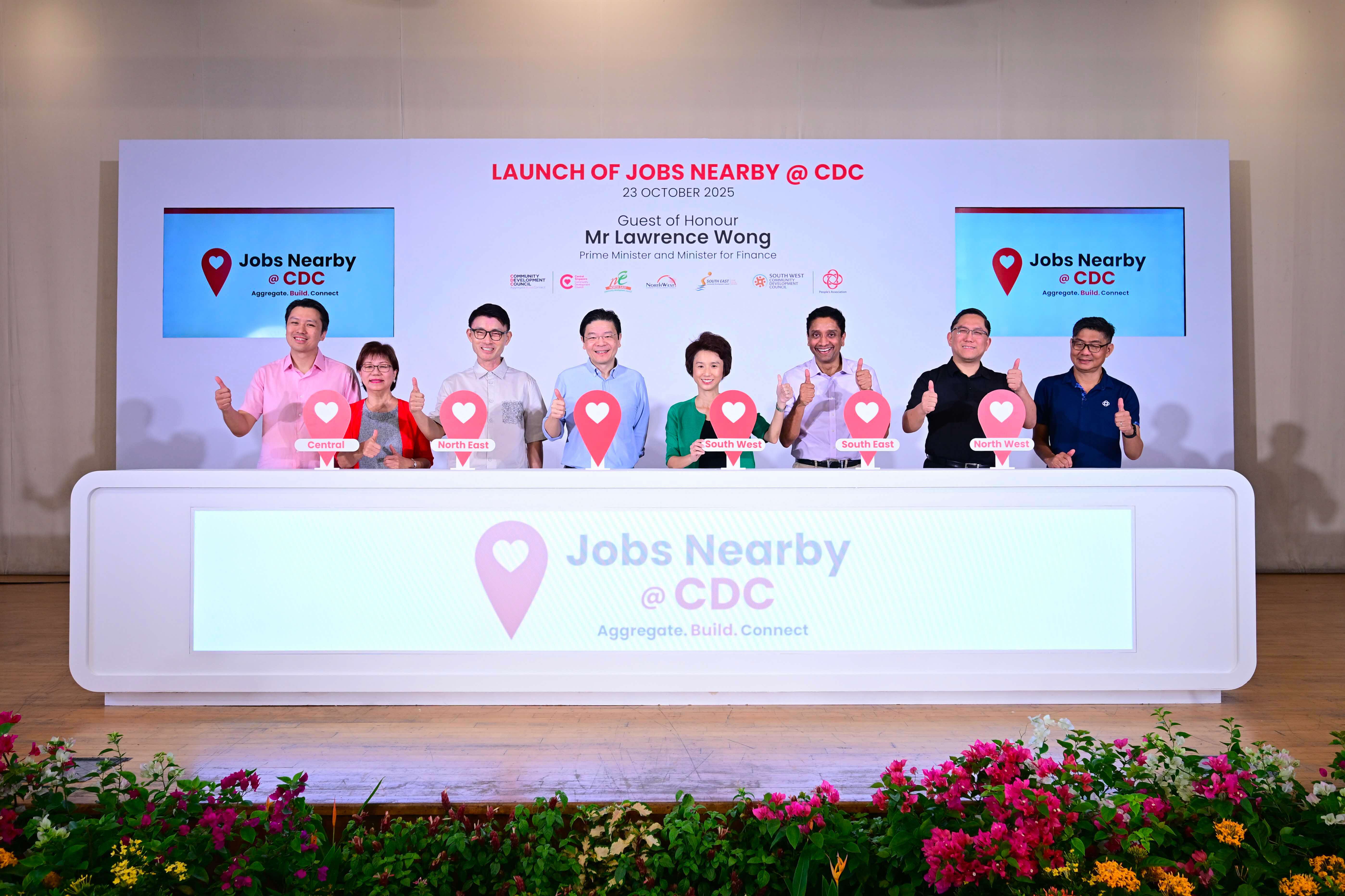Seven people give thumbs-up at the launch event for "Jobs Nearby @ CDC"; each holds signs indicating different regions.