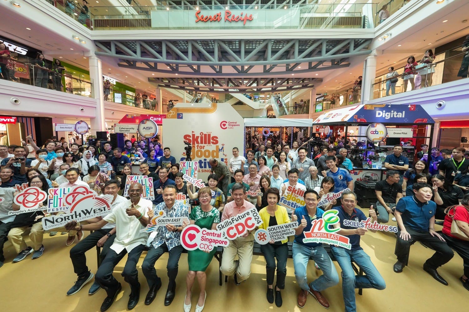 A large group of people holding signs at the Skills for Good festival in a busy shopping mall.