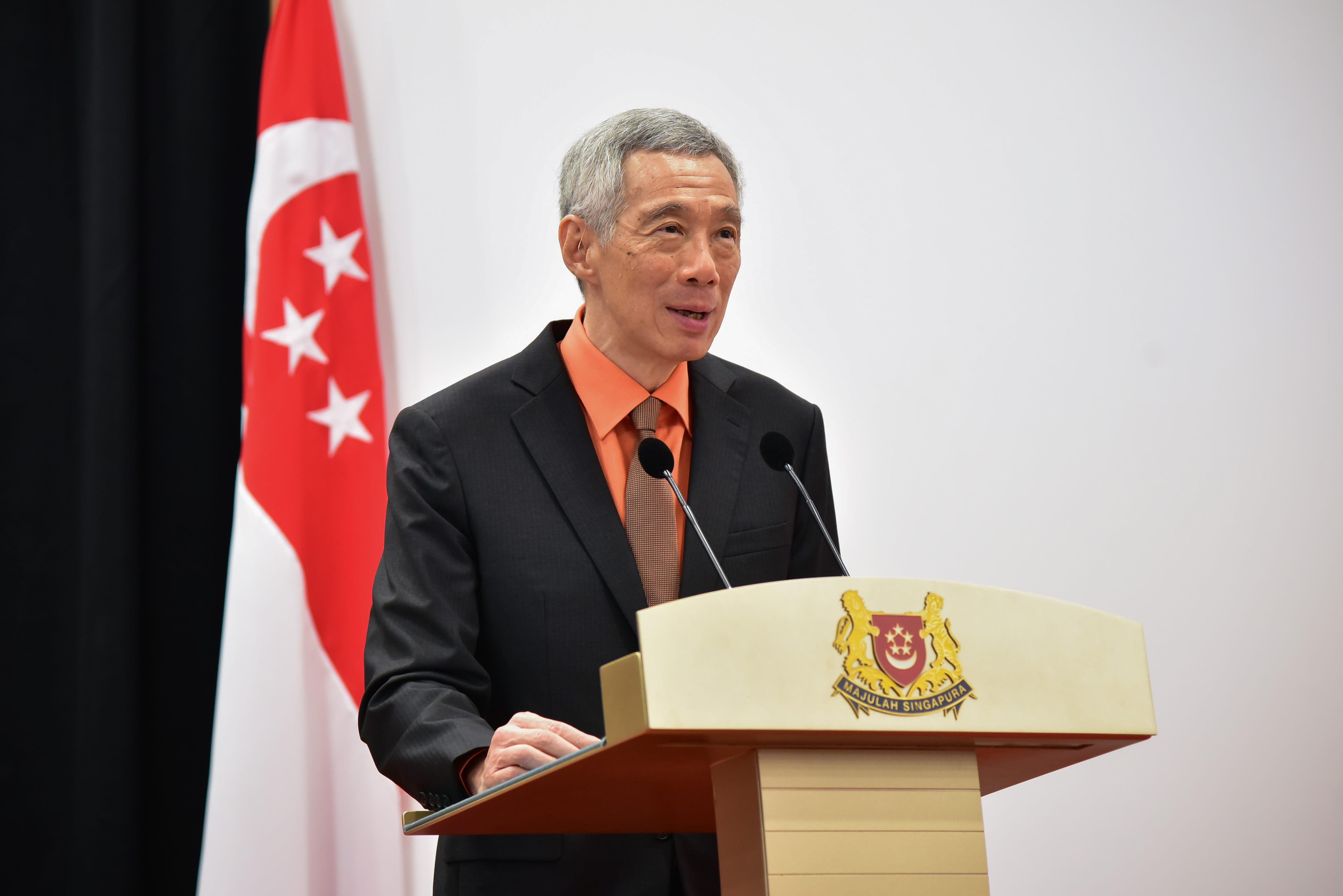 A person is standing at a podium with the emblem of Singapore and a flag in the background.