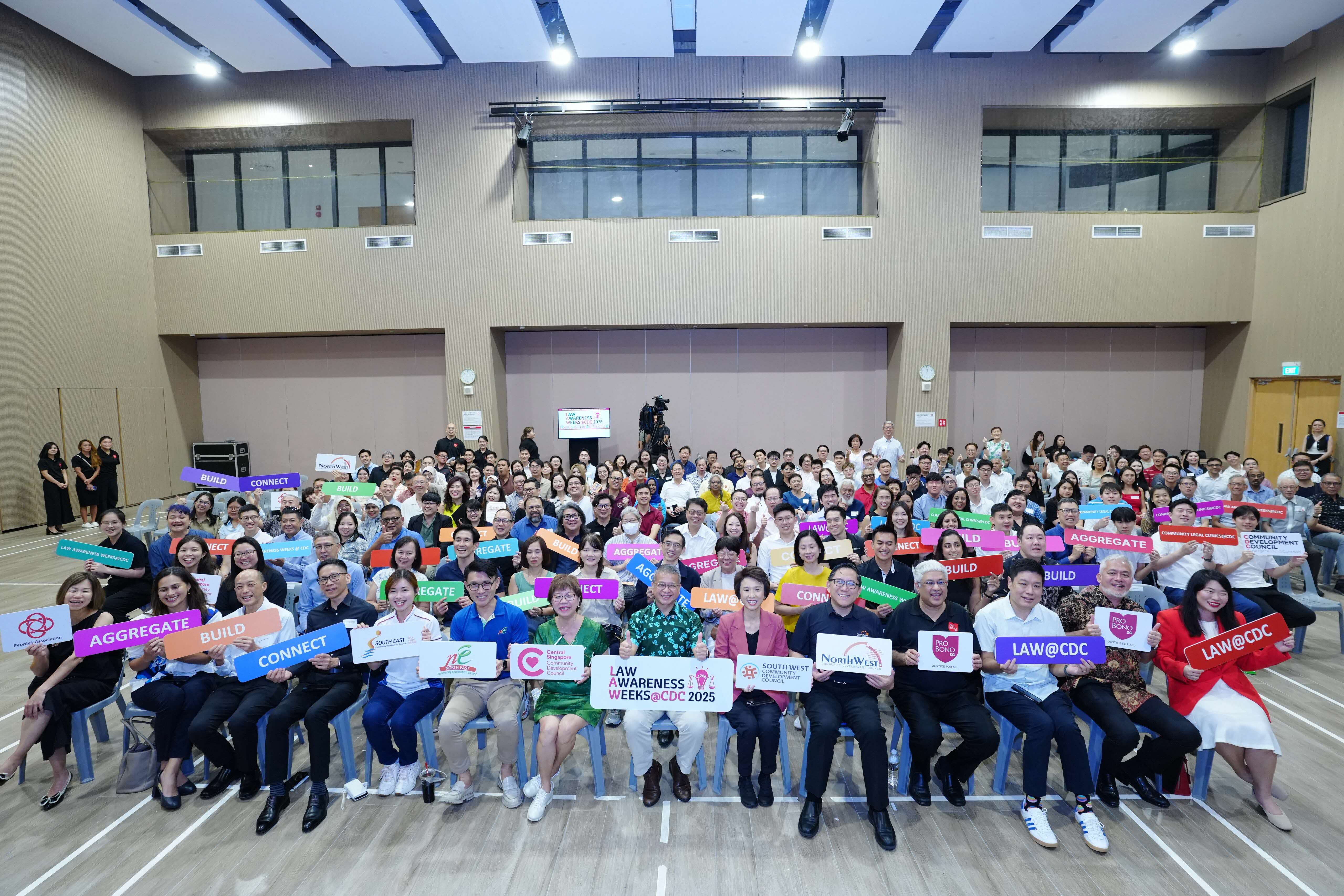 A large group of people in an indoor space holding colorful signs with various words such as "Connect," "Aggregate," and "Build."