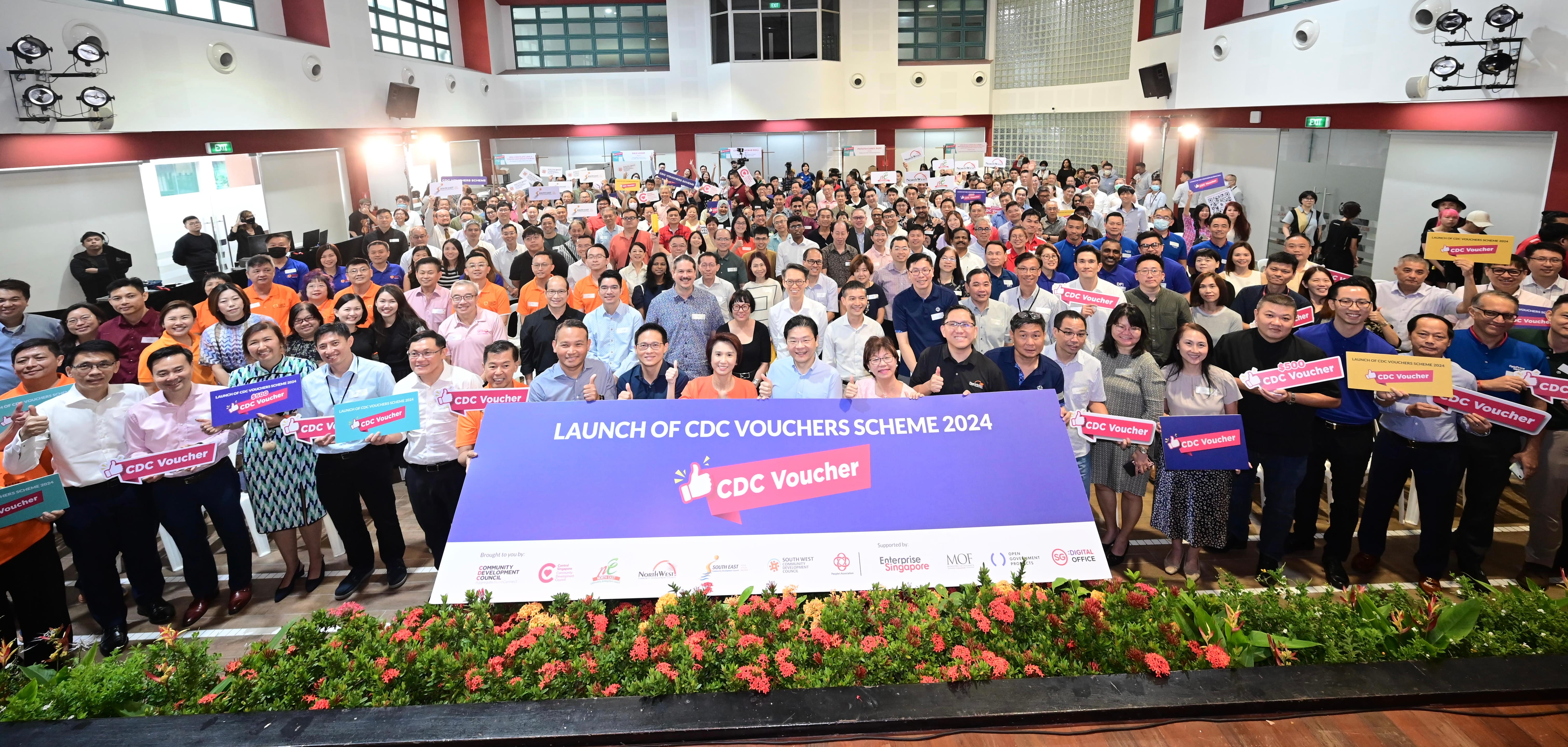 A large indoor event with a crowd holding signs, celebrating the launch of CDC Vouchers Scheme 2024.