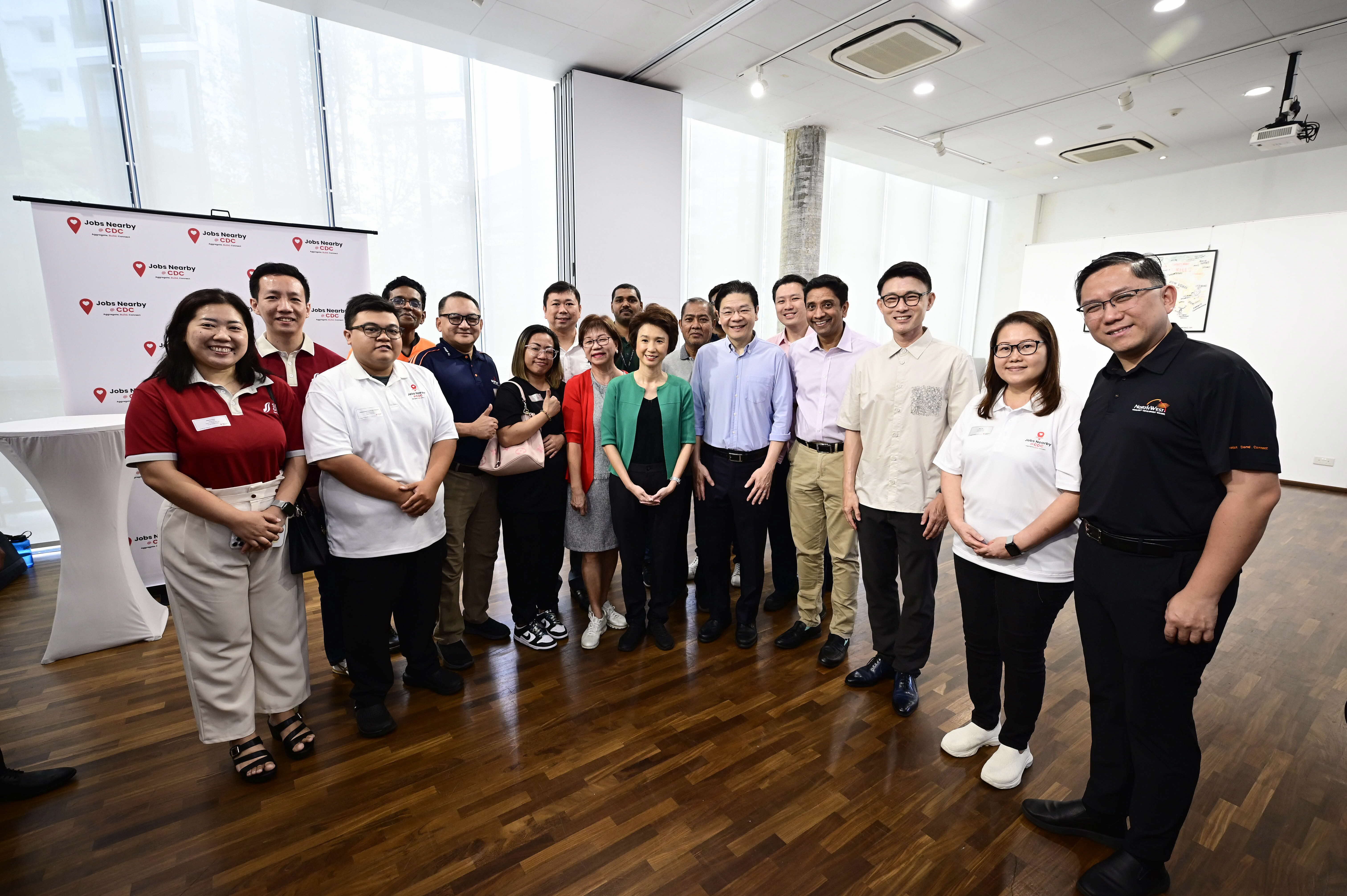 A group of people standing indoors with a sign reading "Jobs Nearby SGUnited" in the background.