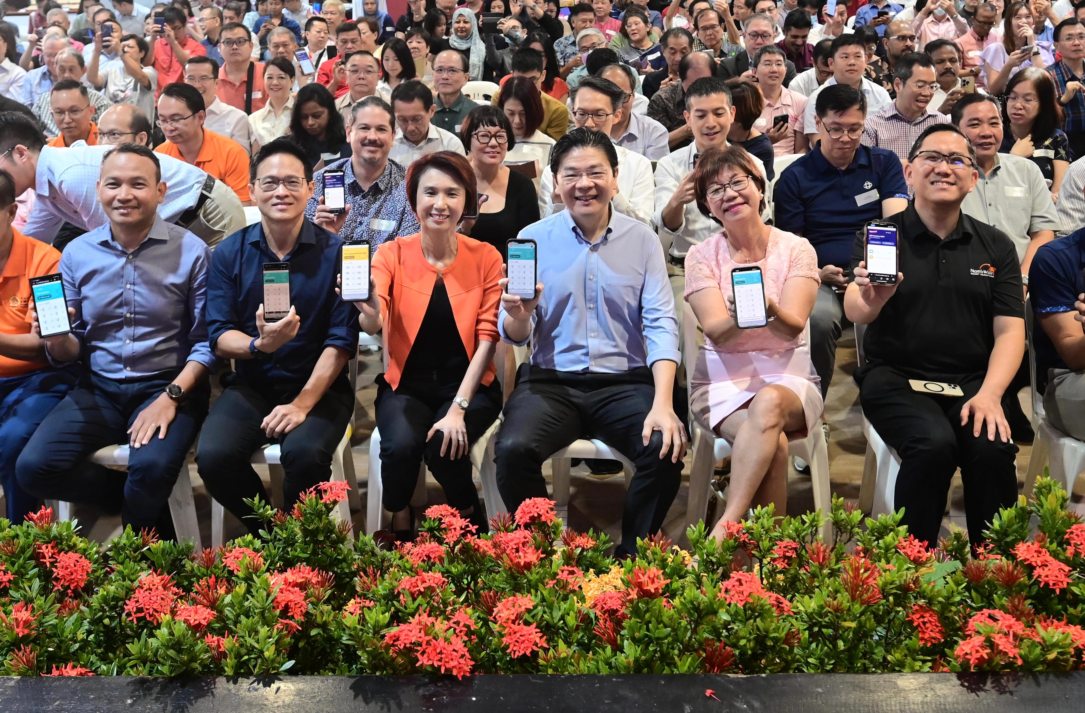Several seated people showing smartphone screens, with red flowers in the foreground.