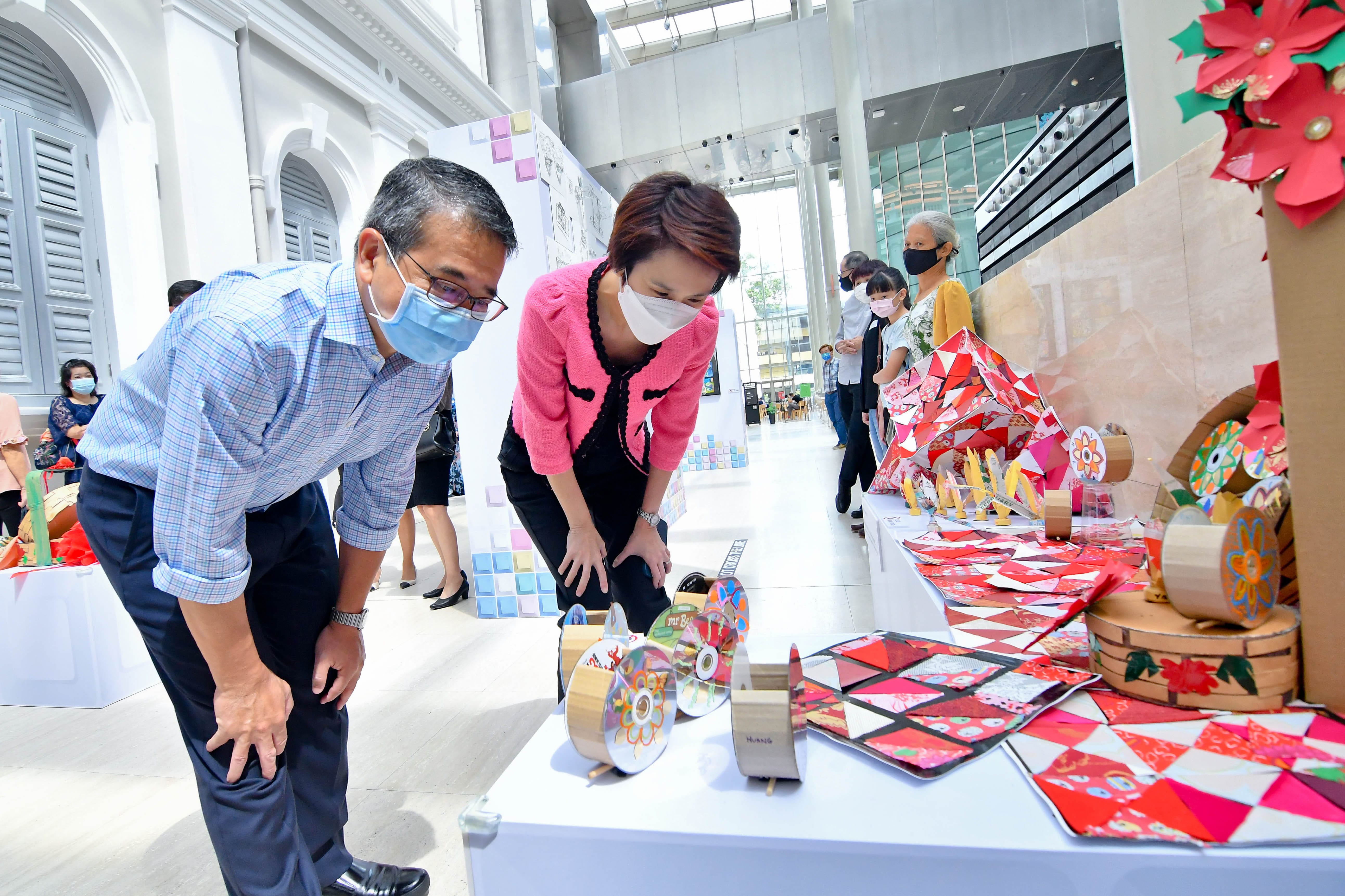 Two people lean over a table displaying colorful craft items in a bright, modern interior setting.