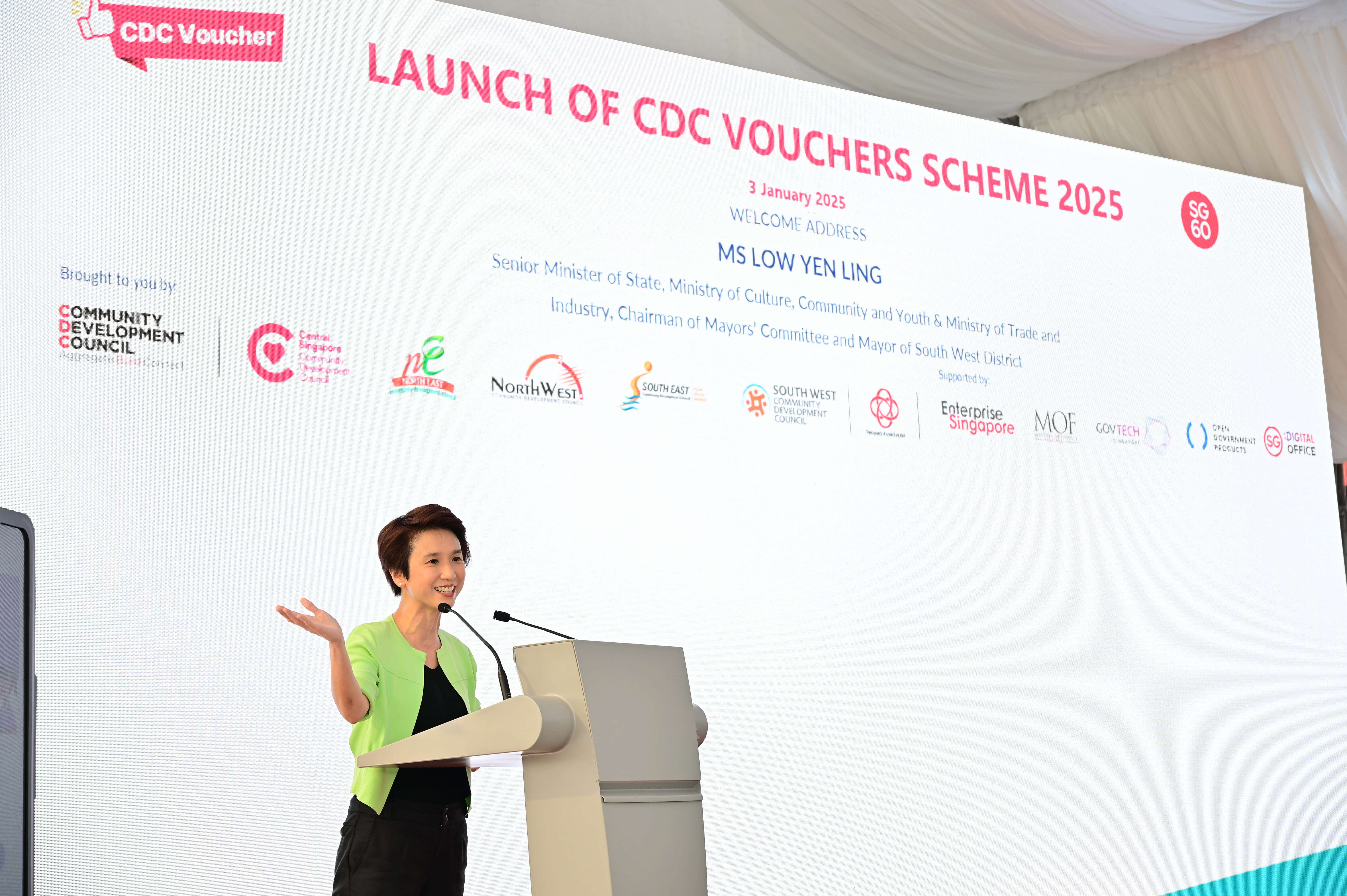 A person stands at a podium speaking at the launch of the CDC Voucher Scheme 2025, with logos of various organizations displayed.