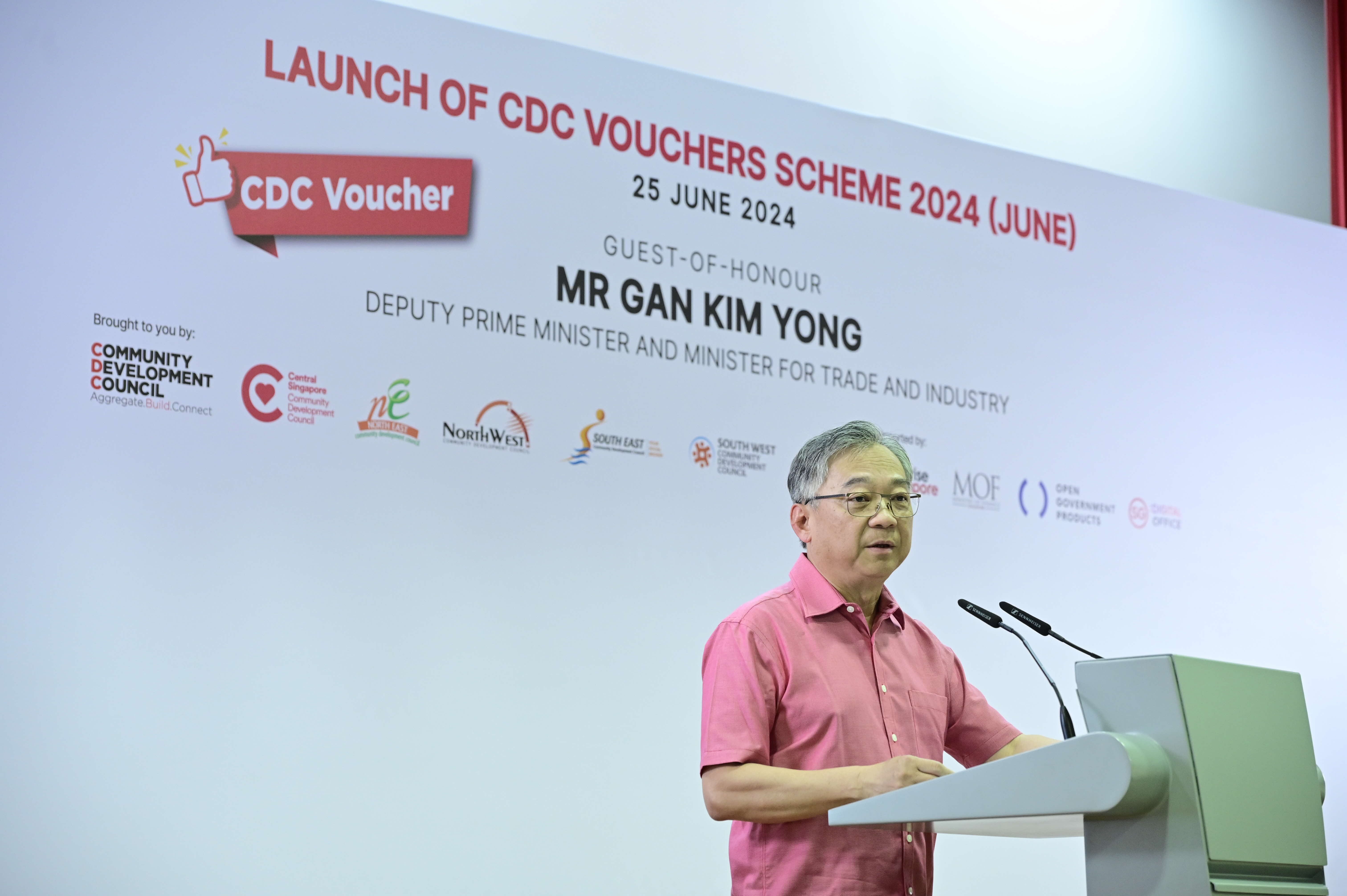 A person in a pink shirt speaks at a podium during the launch of the CDC Vouchers Scheme 2024 event.