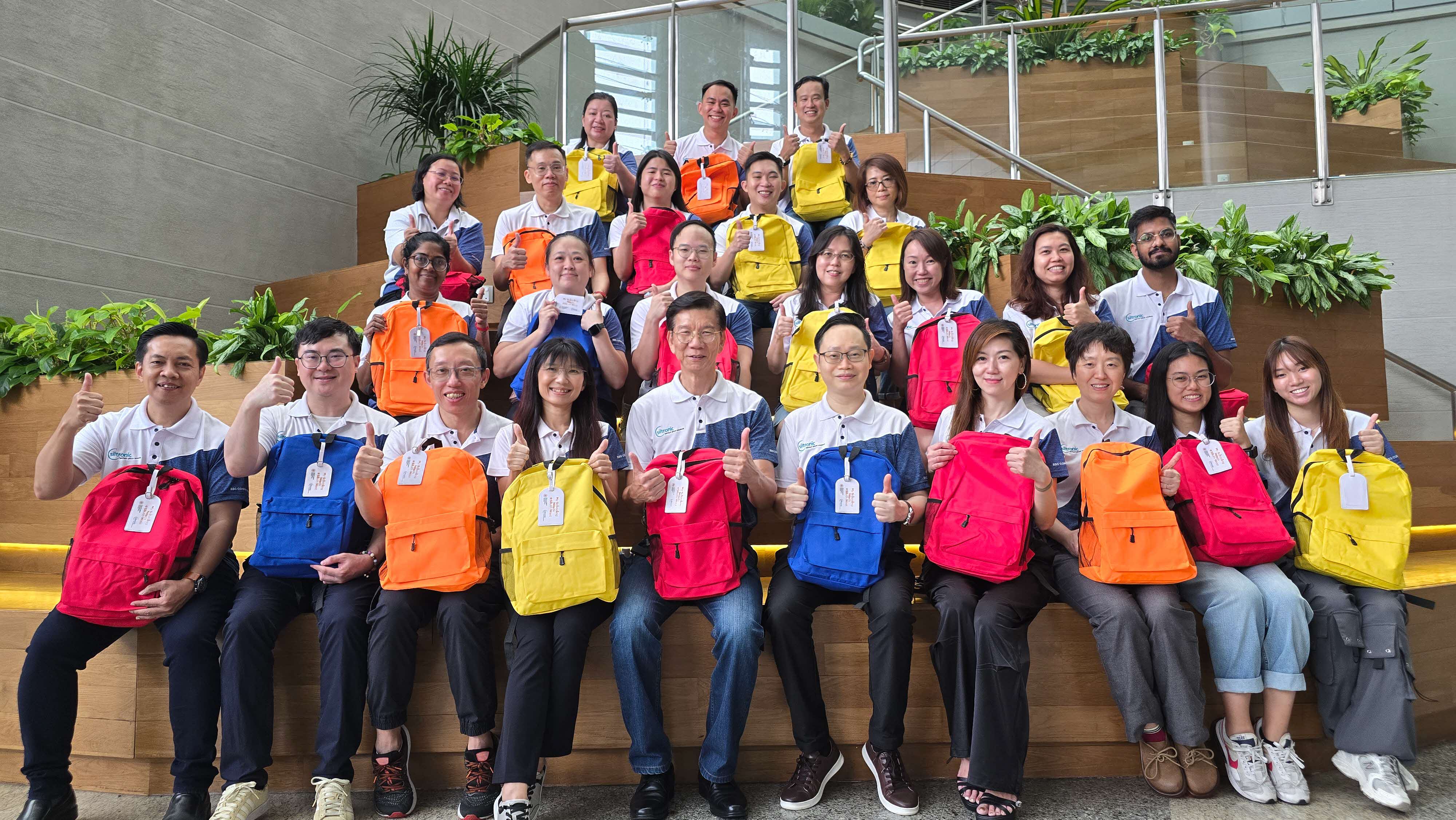 Representatives from corporate partner Siltronic Singapore, carrying colourful backpacks and giving a thumbs up at My Schooling Needs @ South West 2025