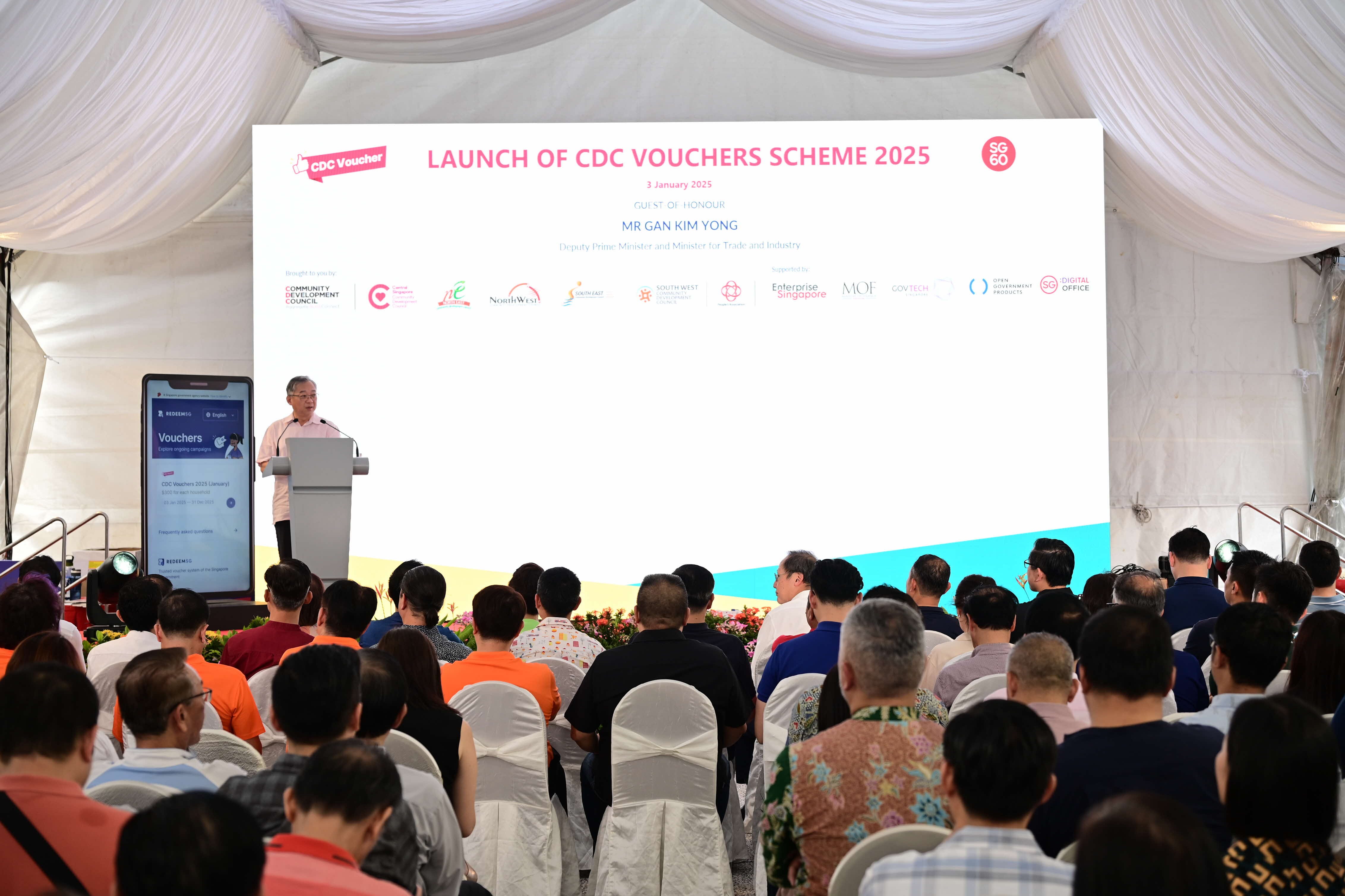 Audience seated facing a stage with a large screen displaying "Launch of CDC Vouchers Scheme 2025".