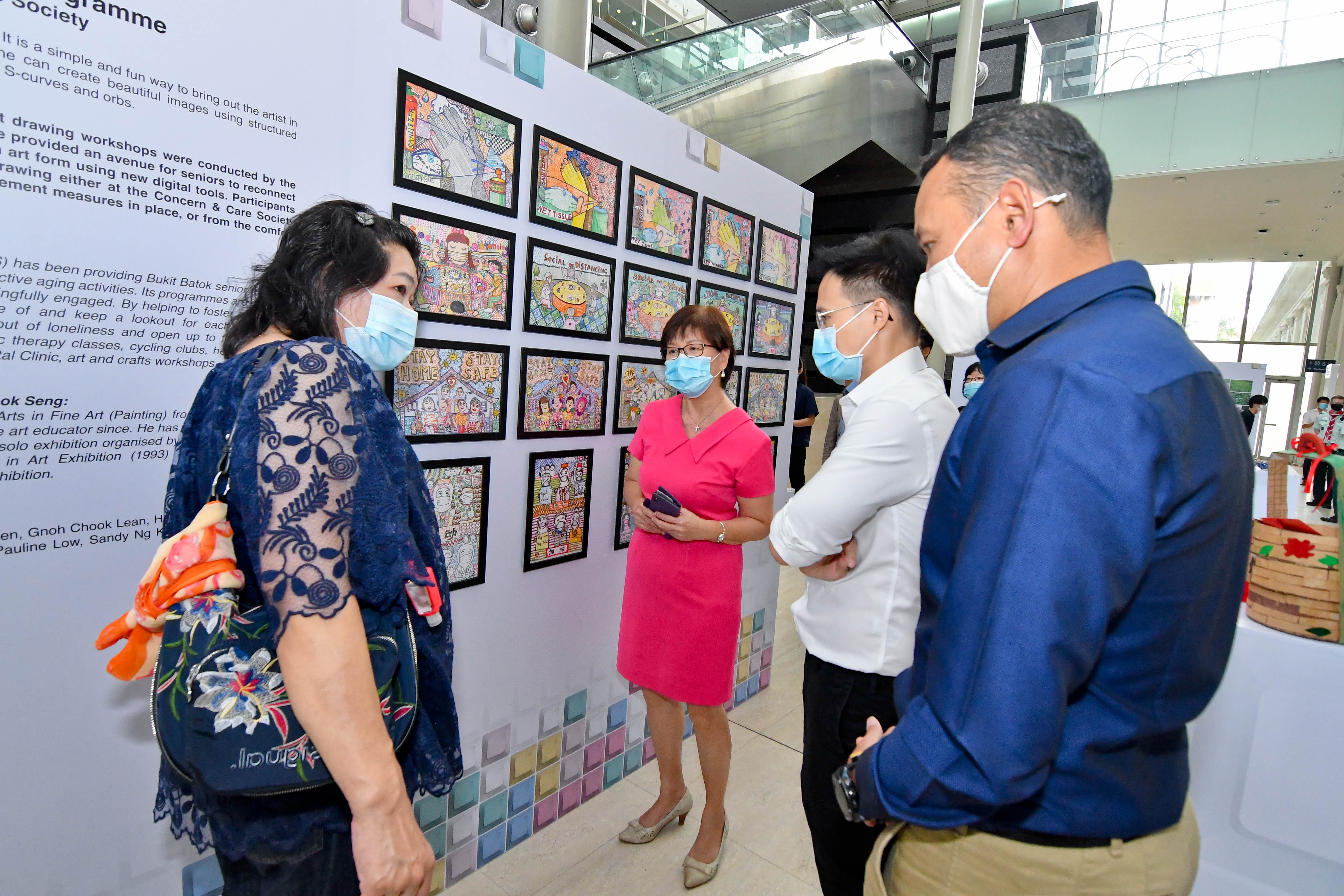 Several people are gathered in front of a wall displaying multiple colorful framed artworks in a modern setting.