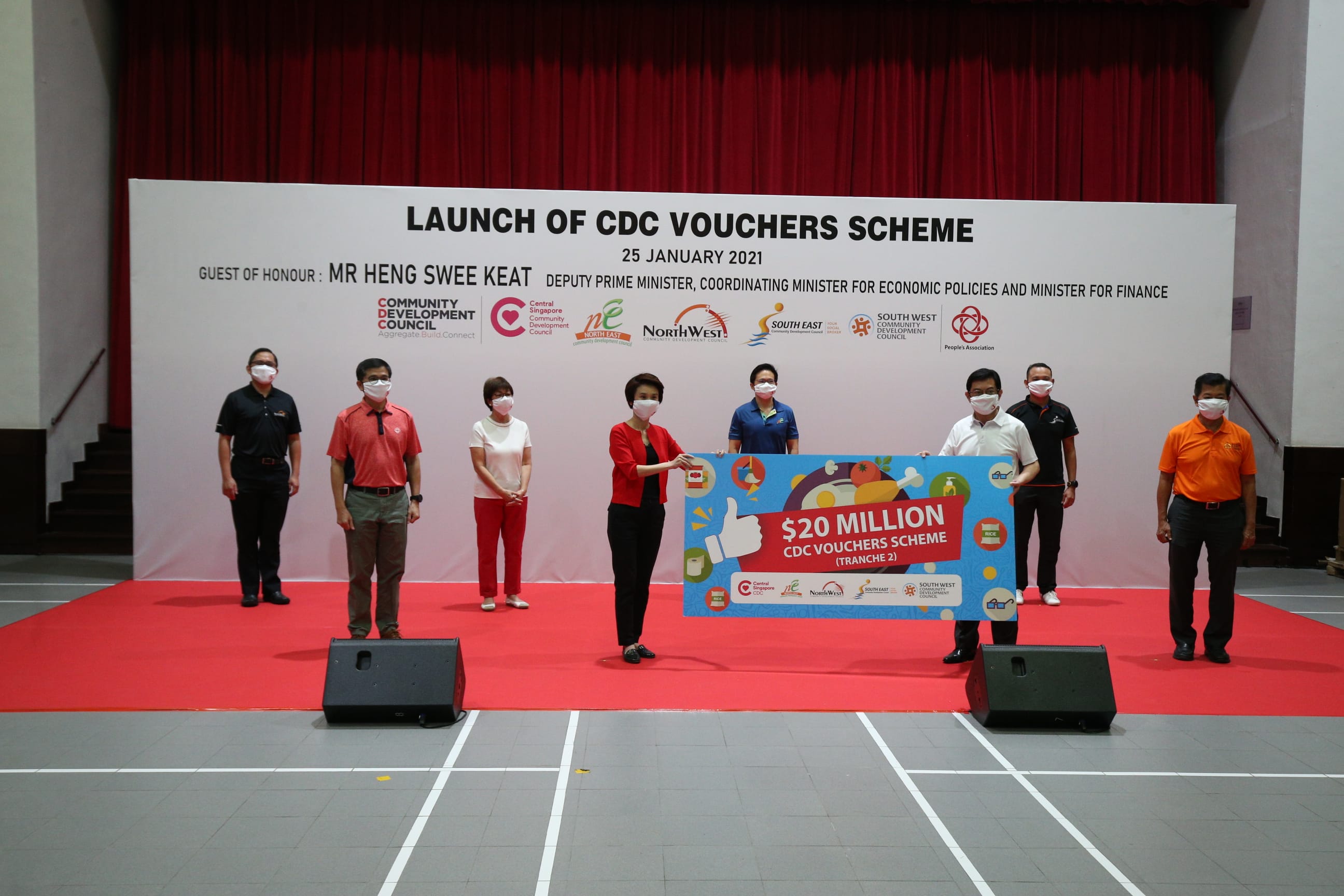 Several people stand on a stage holding a large placard for $20 million CDC voucher scheme launch on January 25, 2021.