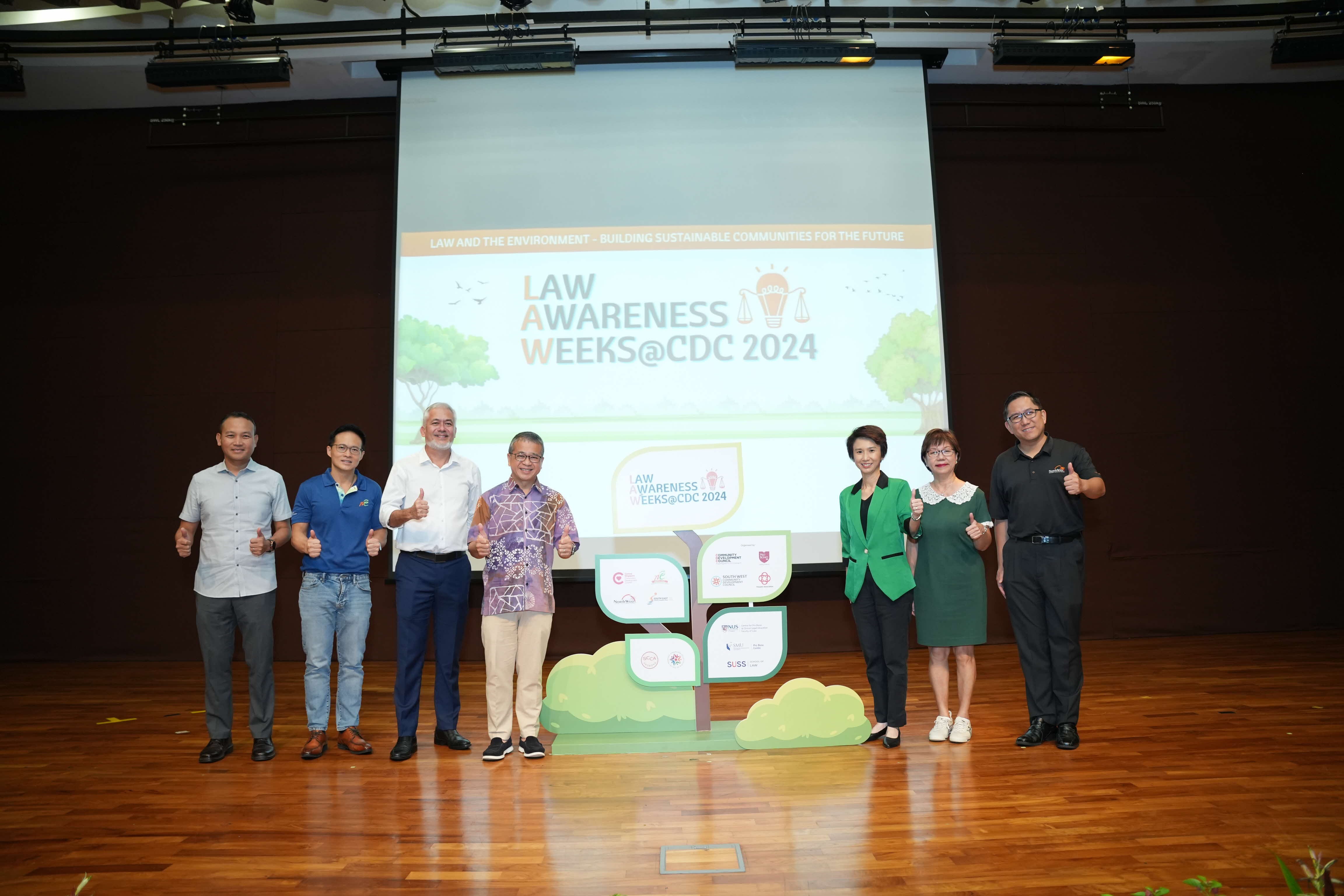 Seven people standing on a stage with a "Law Awareness Weeks@CDC 2024" banner in the background.