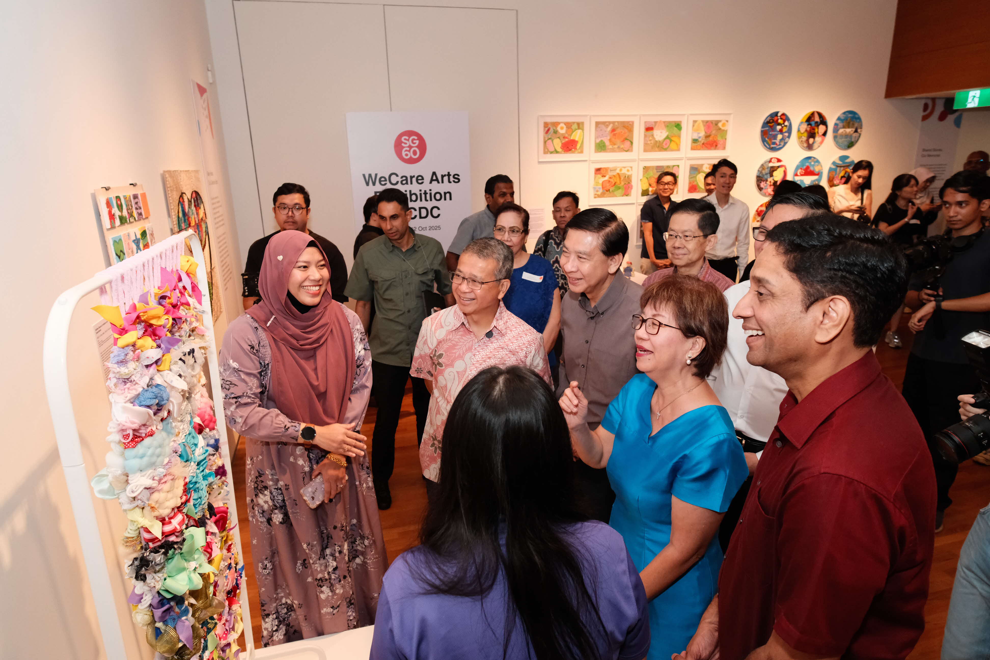 People gather at an art exhibition, with various artworks displayed on the walls and a fabric sculpture in the foreground.