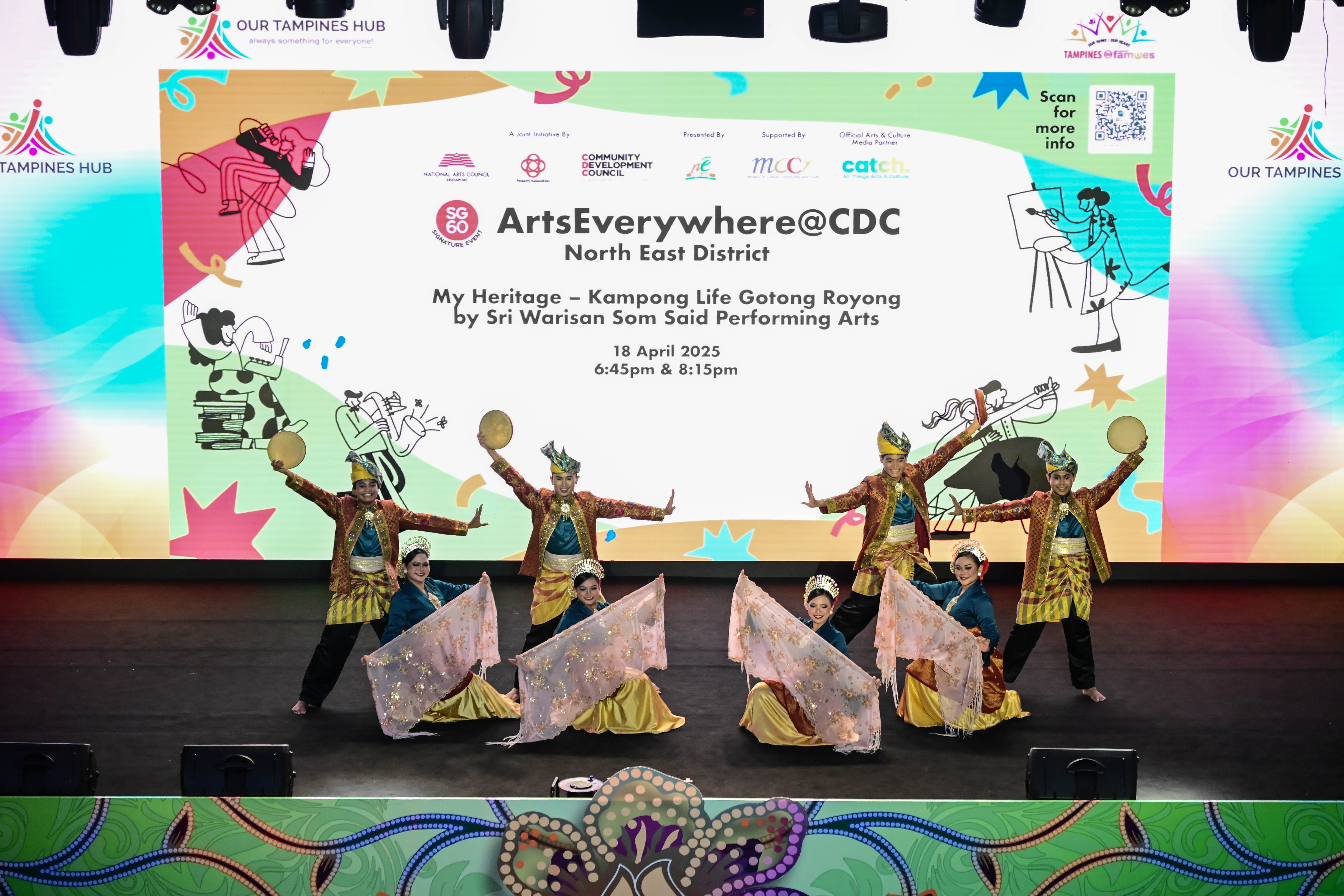 A group of performers in traditional attire are dancing in front of a brightly colored event backdrop.