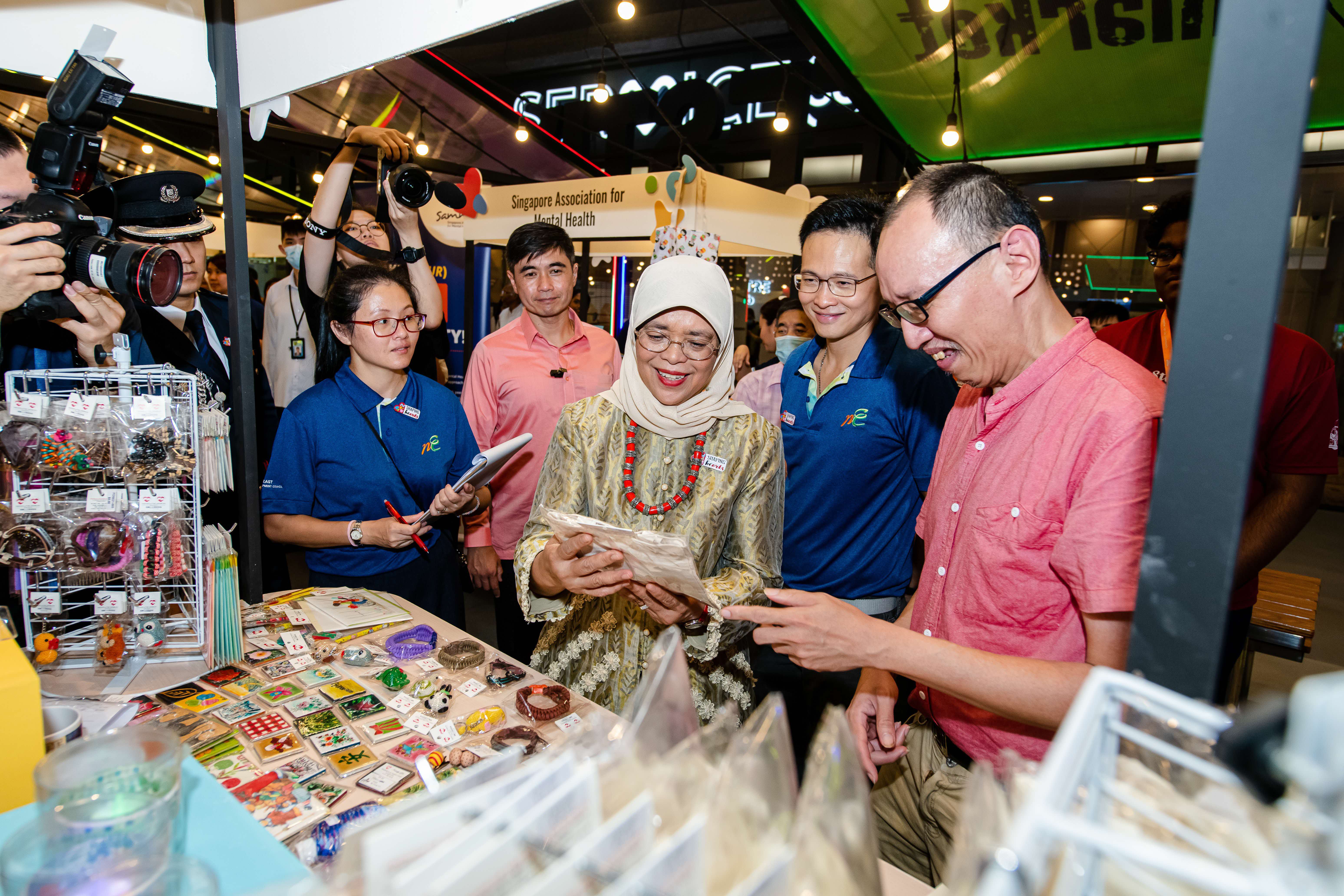 A group of people gather around a table displaying various colourful items at Shaping Hearts event booth.