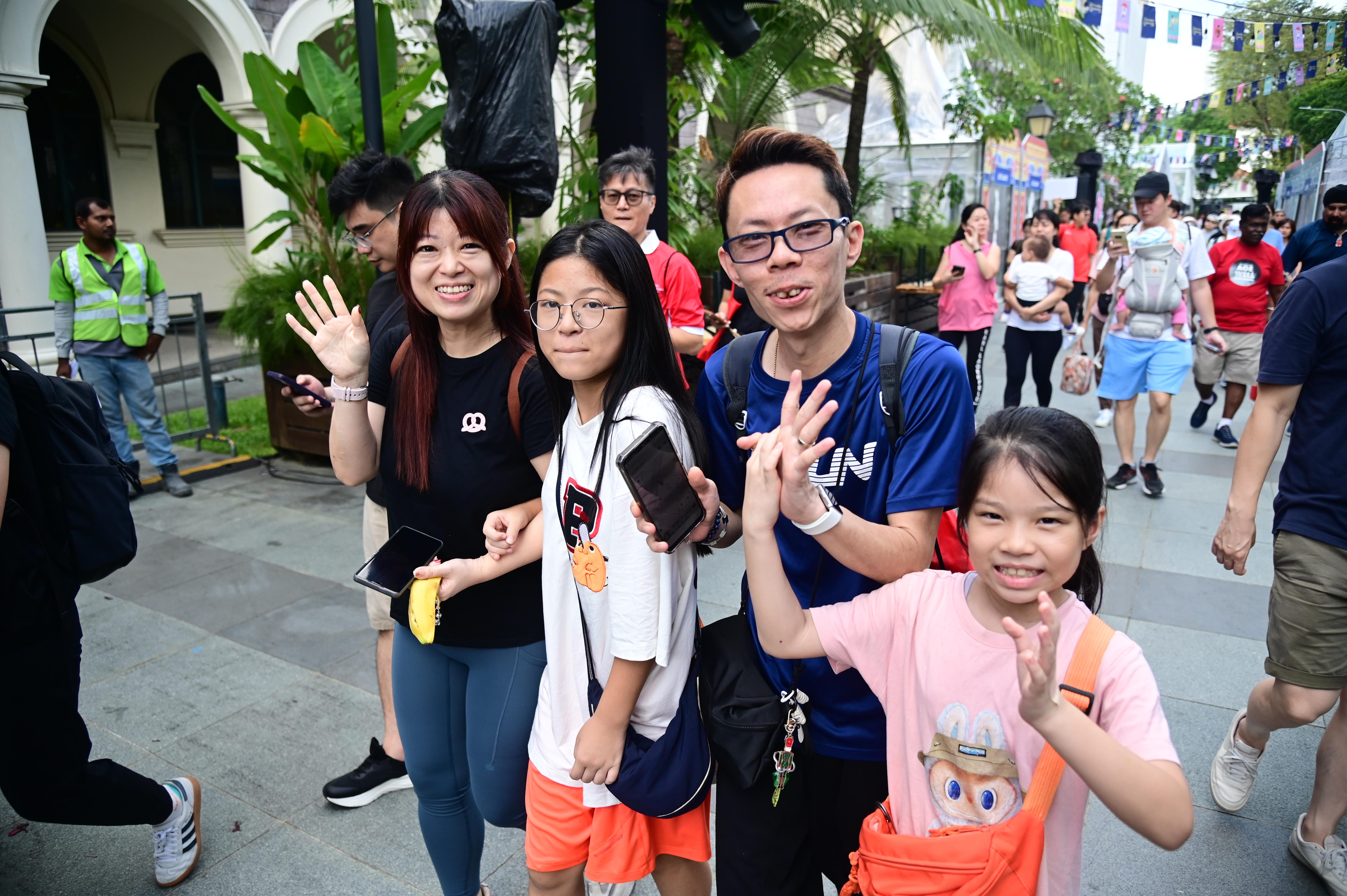 Family and participants smiling and waving during a community walk or outdoor event.