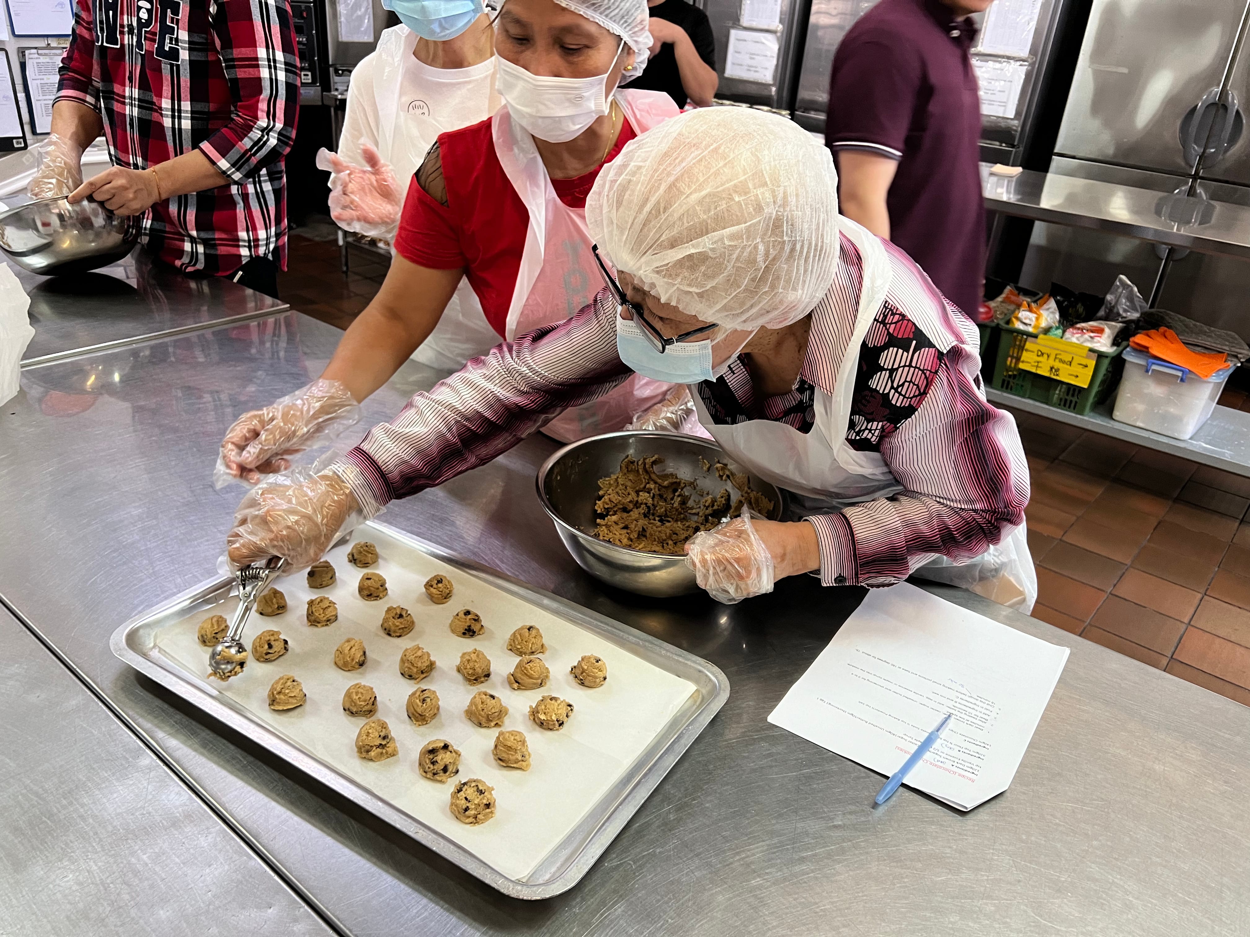 A woman scooping portions of cookie dough onto a baking tray lined with parchment paper.