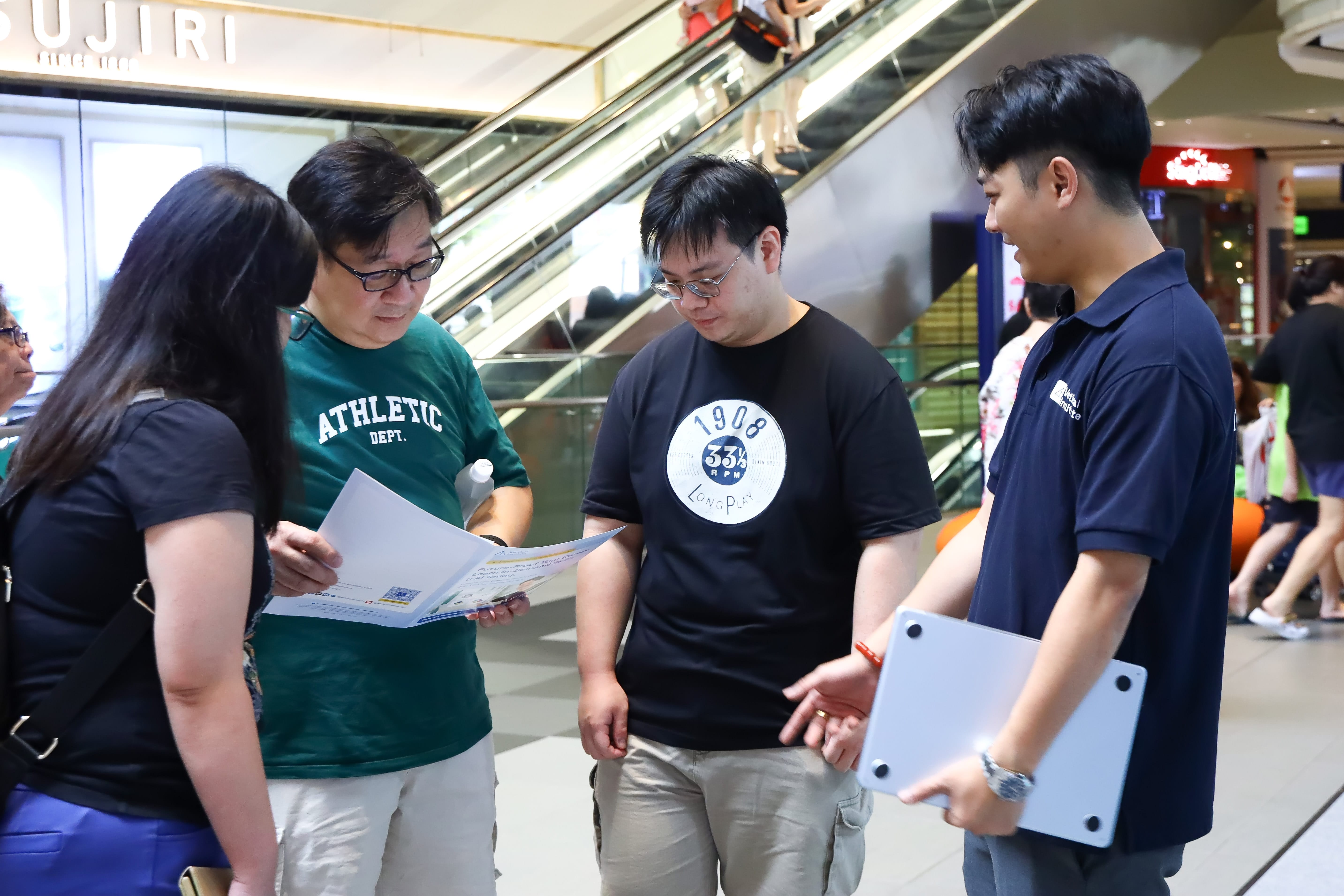 2 men a woman speaking with a staff member at the Career Fest reviewing informational materials about a programme or activity.