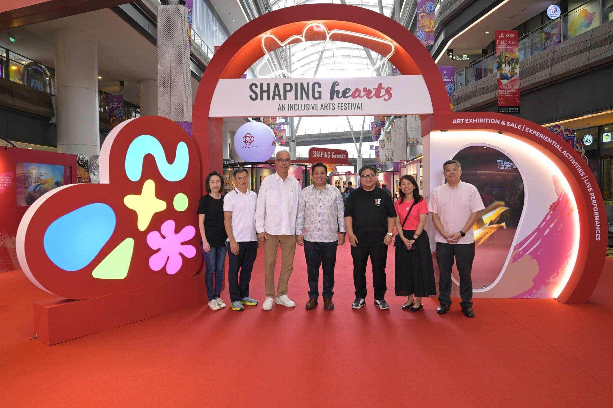 Group photo of people standing at the entrance of the Shaping Hearts inclusive arts festival, held in a mall setting. 
