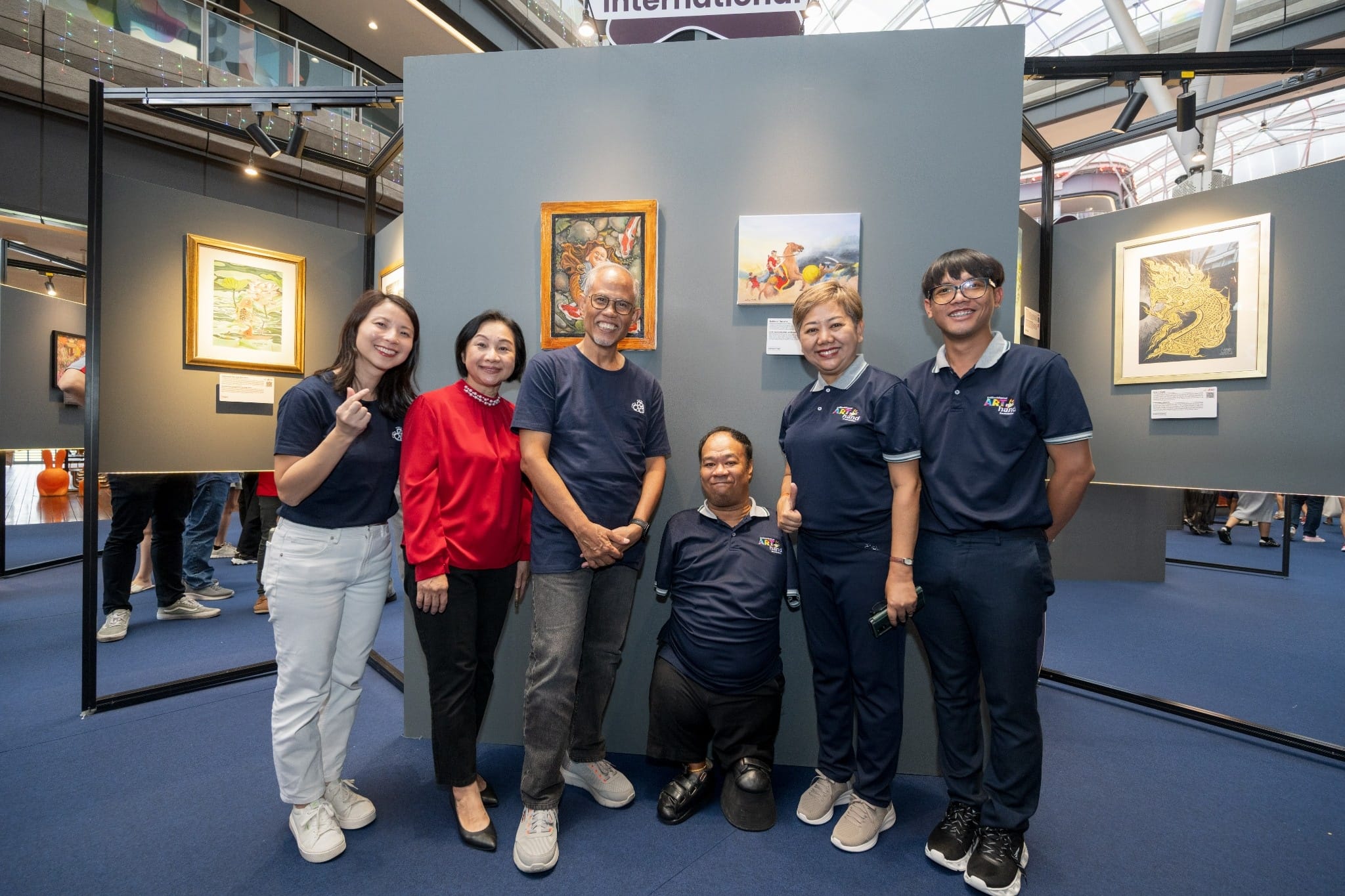 A group photo of participants posing together at an art exhibition showcasing framed artworks.