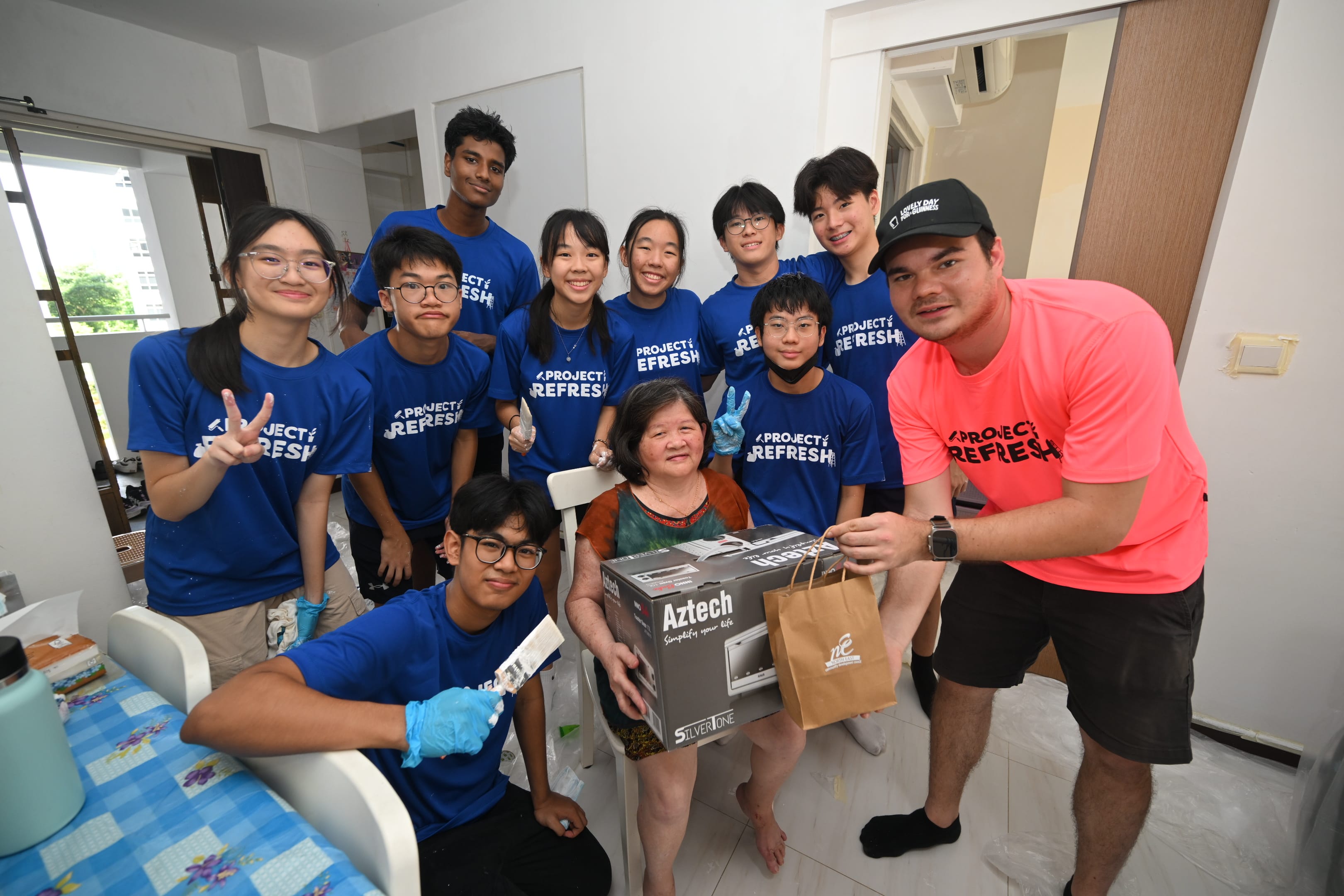 Volunteers visiting a resident at home as part of Project Refresh, presenting household items and support while working on a home improvement project.