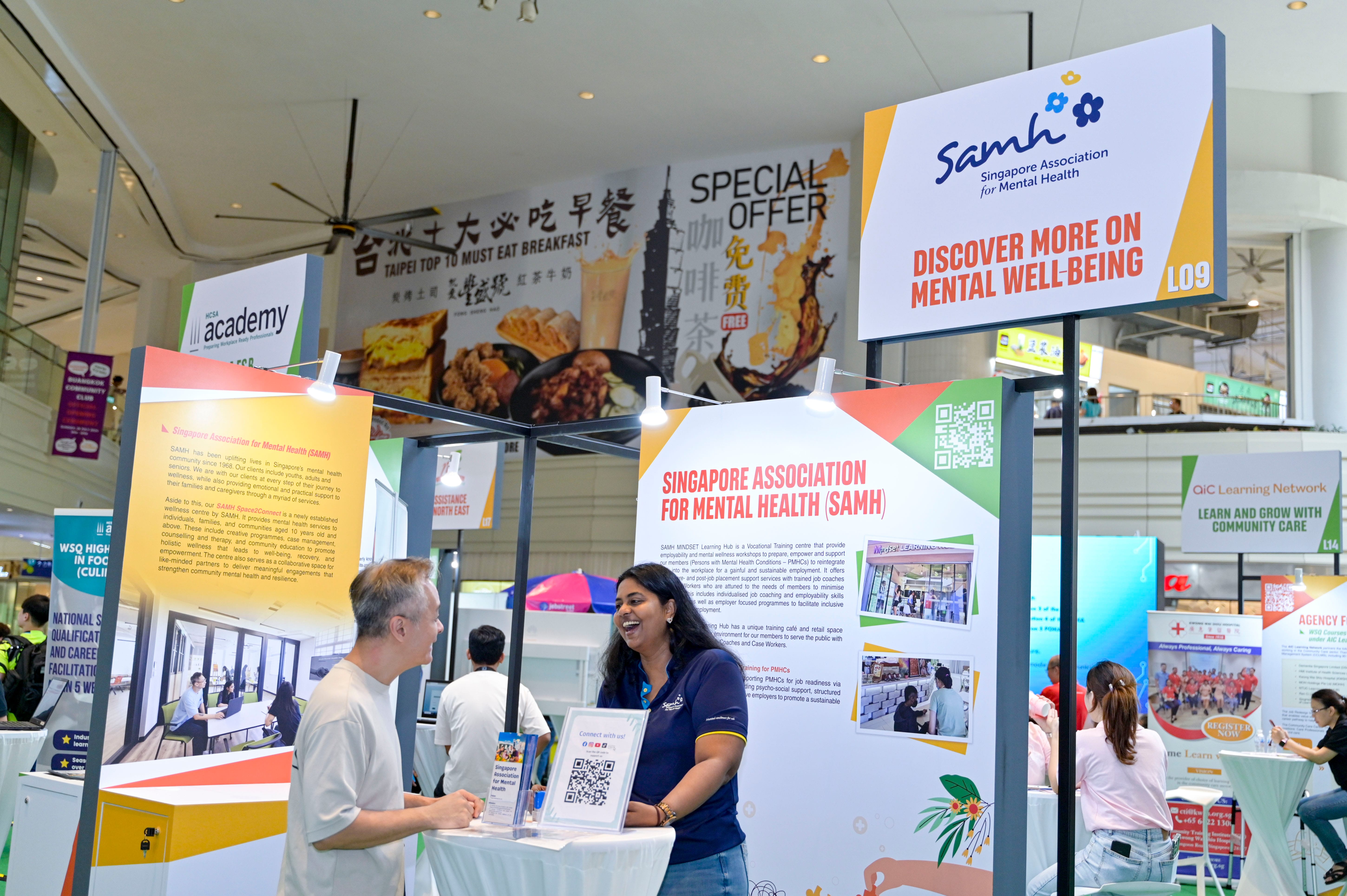 A person engages with a representative at a Singapore Association for Mental Health (SAMH) booth in a mall.