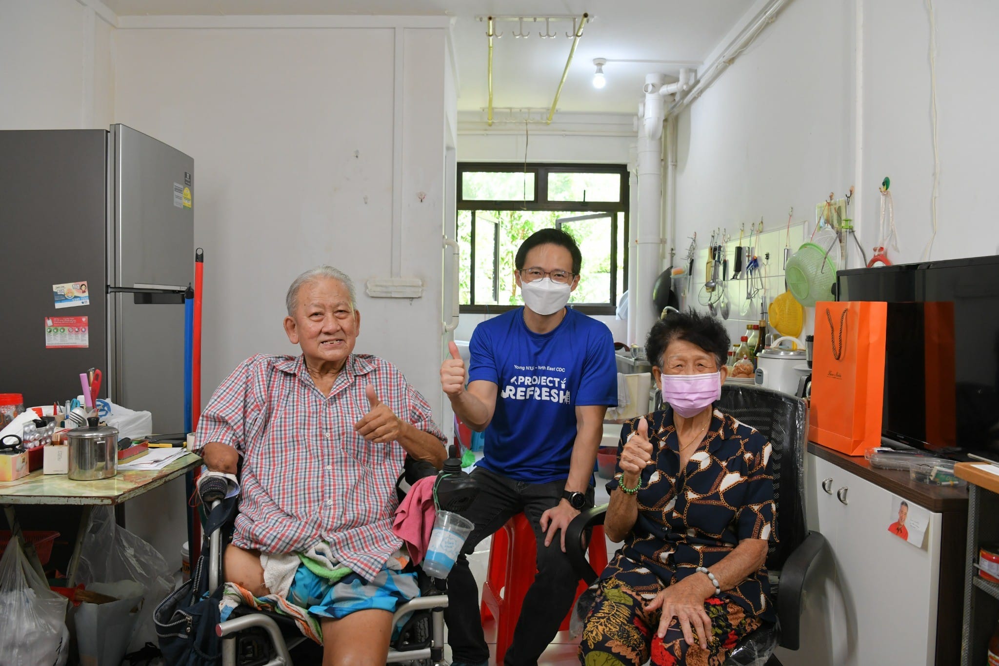 A man visiting two elderly residents at home, posing together in their home.