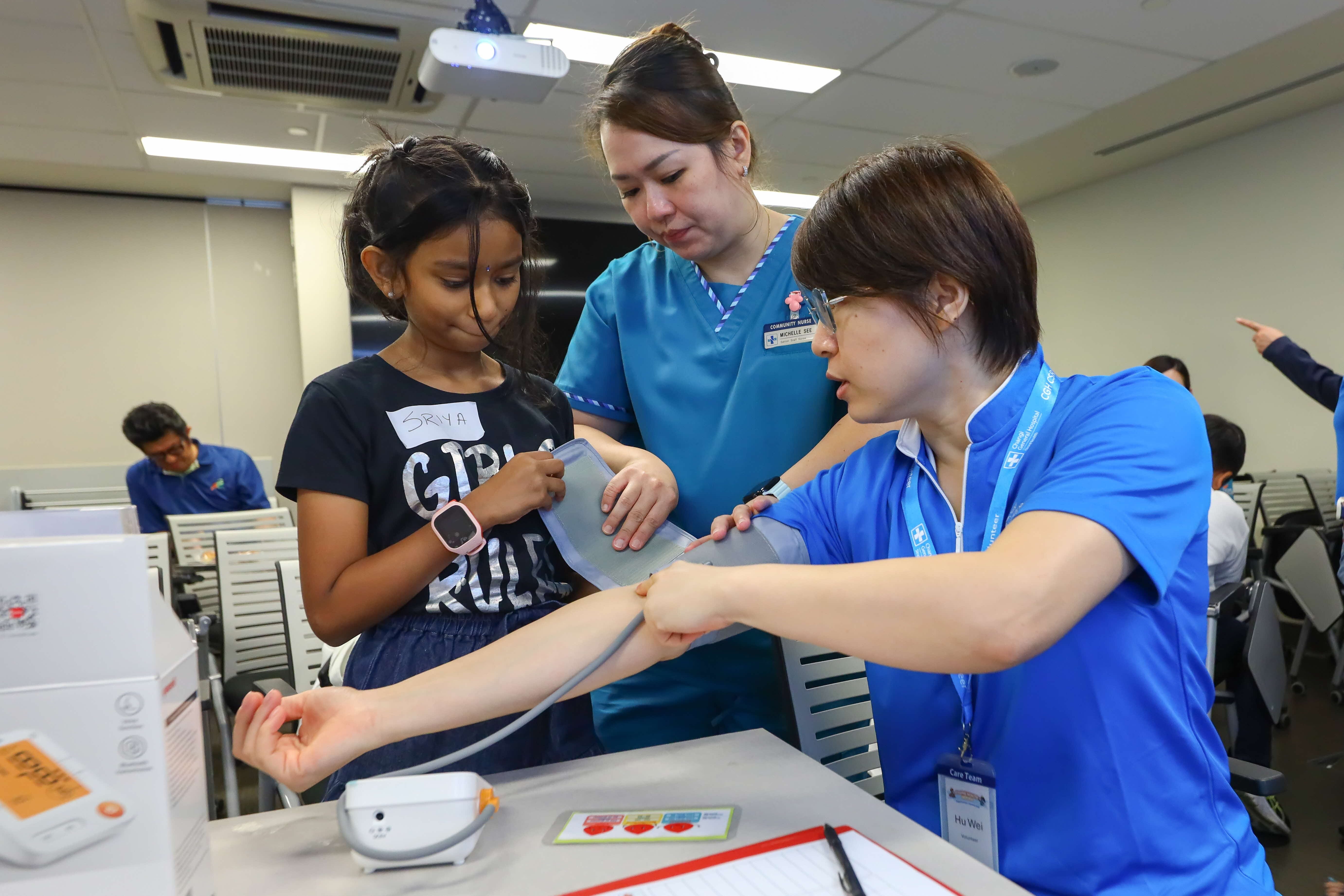 Young participant learns how to measure blood pressure with guidance from healthcare professionals at Changi General Hospital.