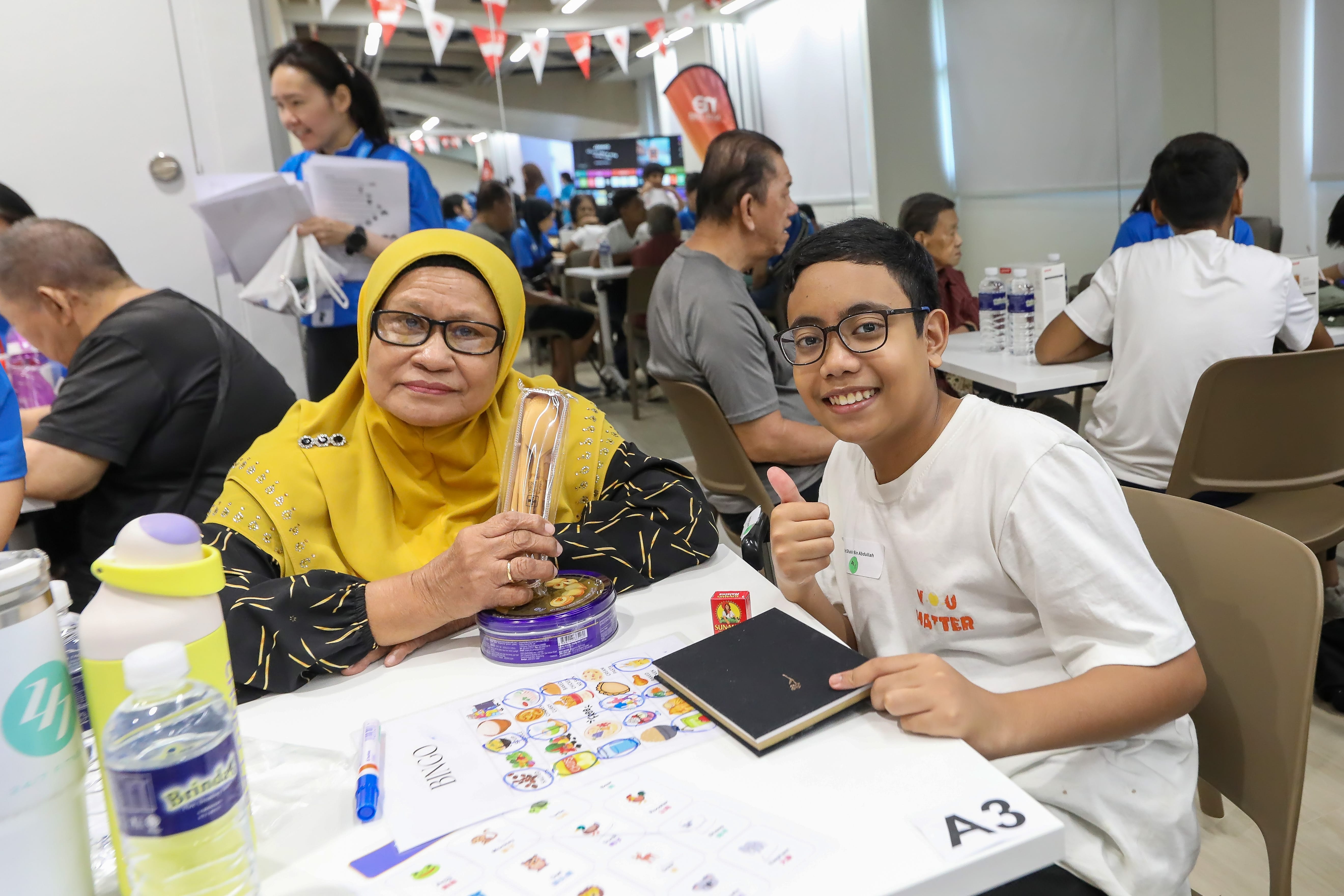 Young Health Hero smiling and giving a thumbs-up while seated beside a senior during an intergenerational activity.