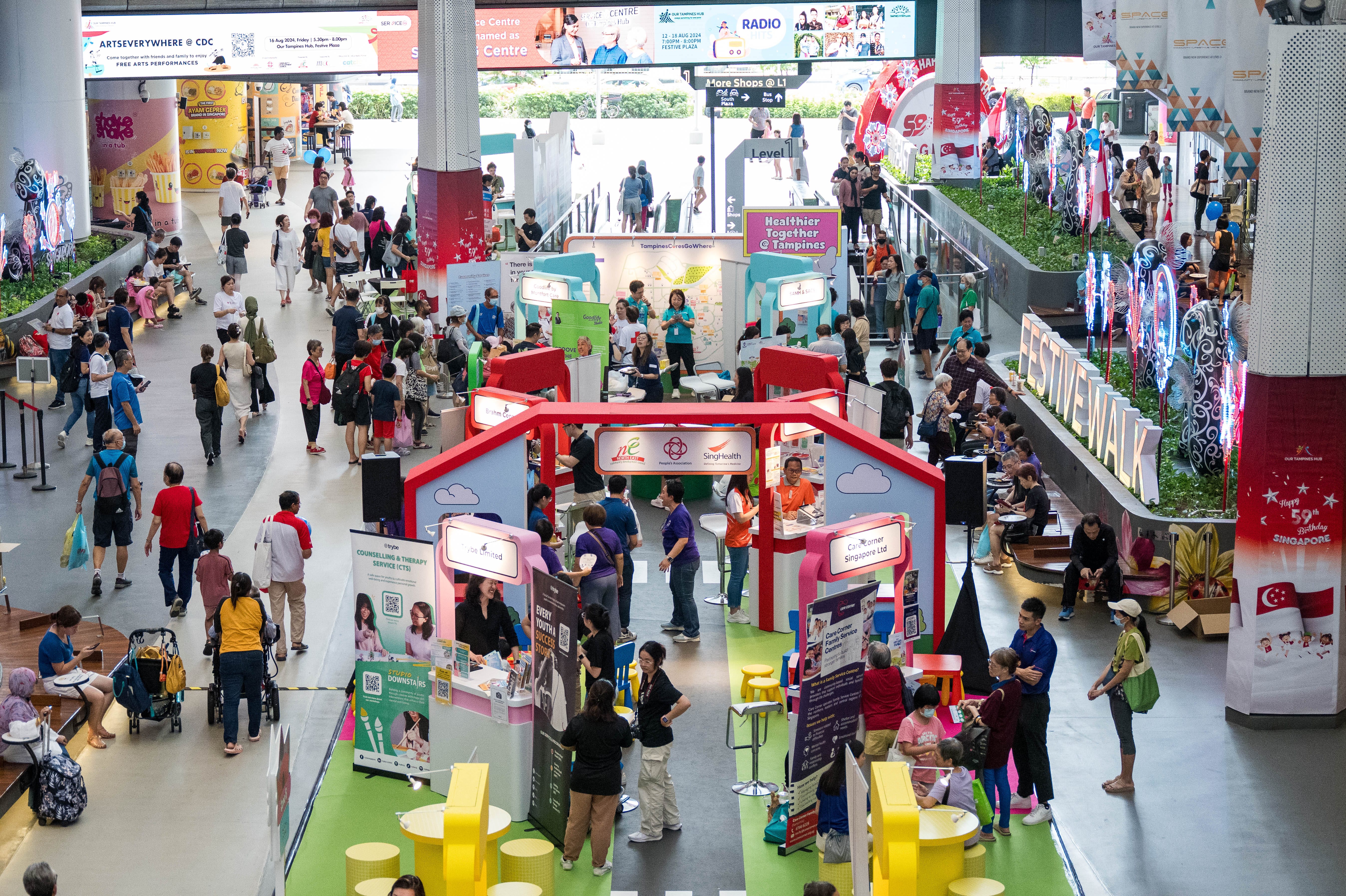 A busy indoor event with multiple booths, informational displays, and people walking around and engaging with exhibitors.