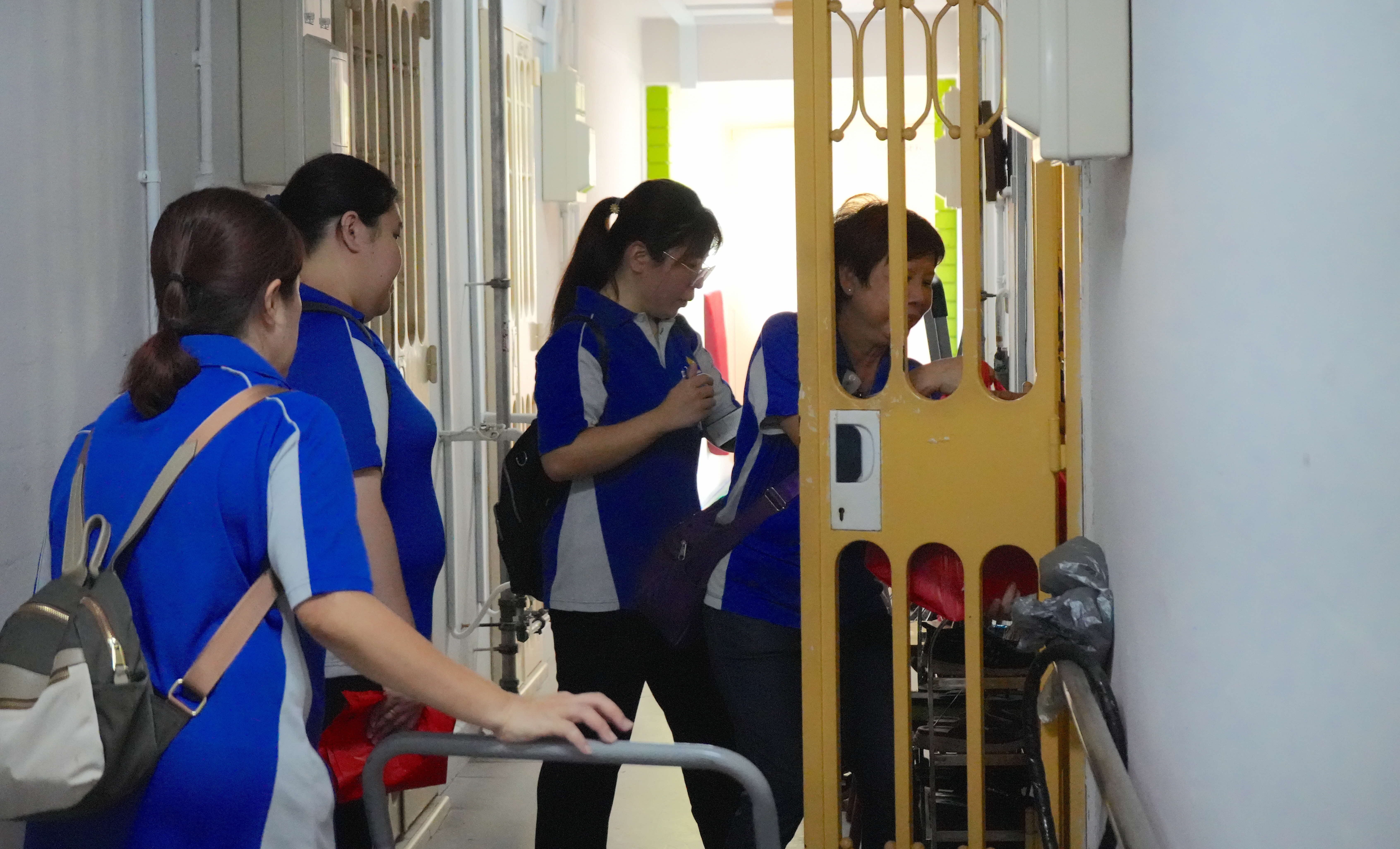 Three people in blue uniforms are gathered near a yellow gate in a narrow indoor corridor.