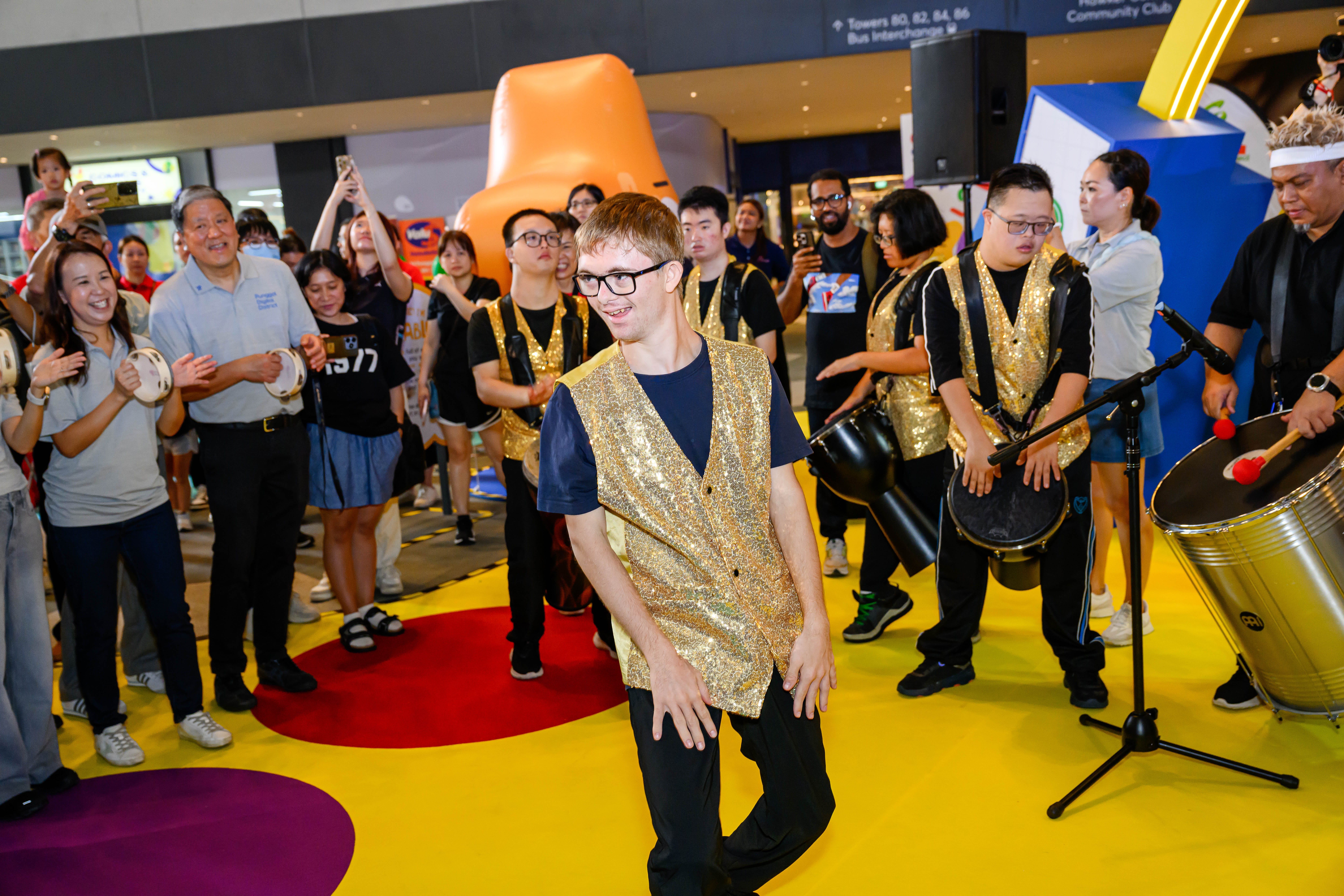 Dancer performing in the center, surrounded by fellow performers at the back and audience members in front.
