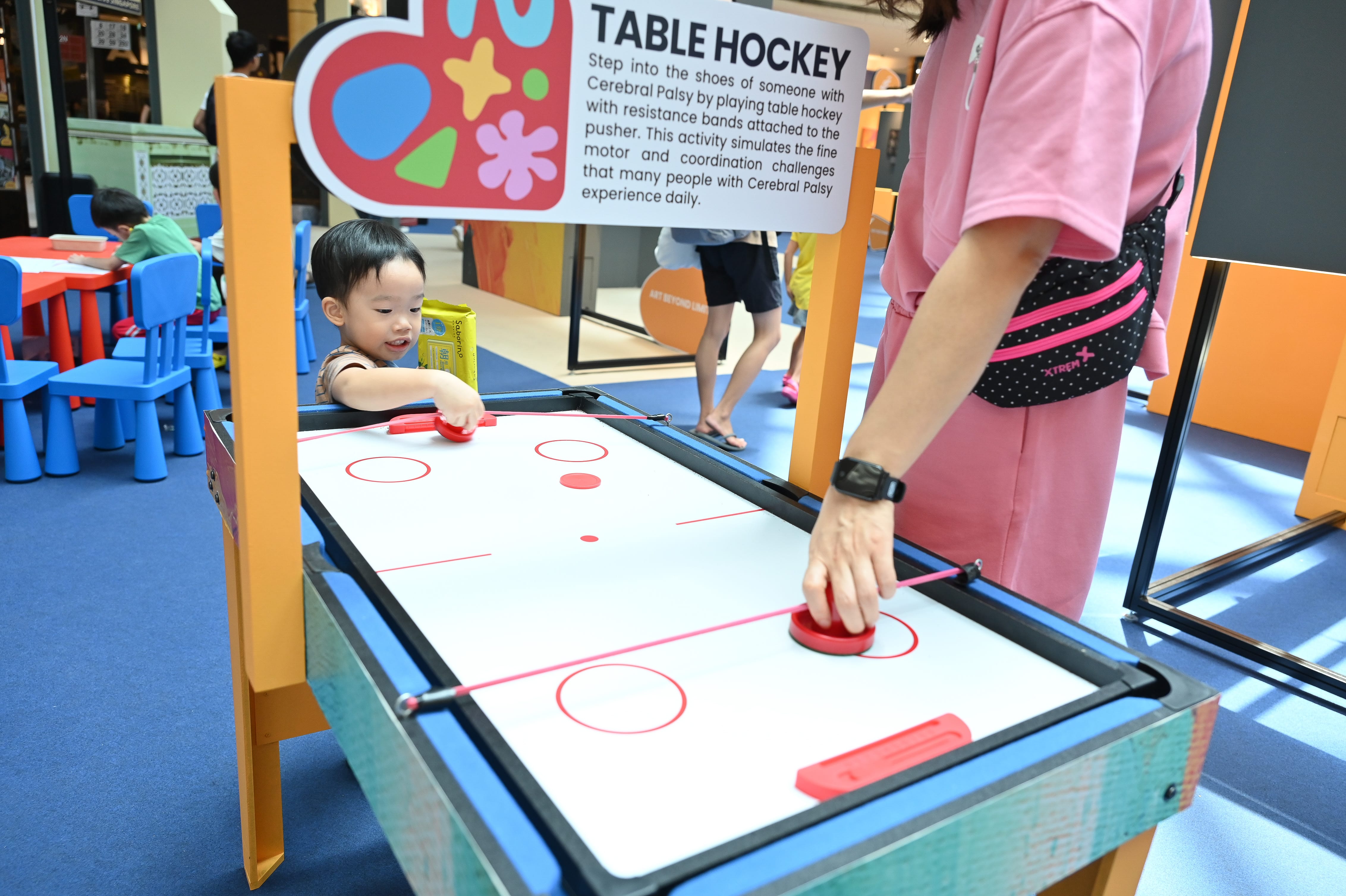 Two people play table hockey with resistance bands at an educational exhibit about cerebral palsy.